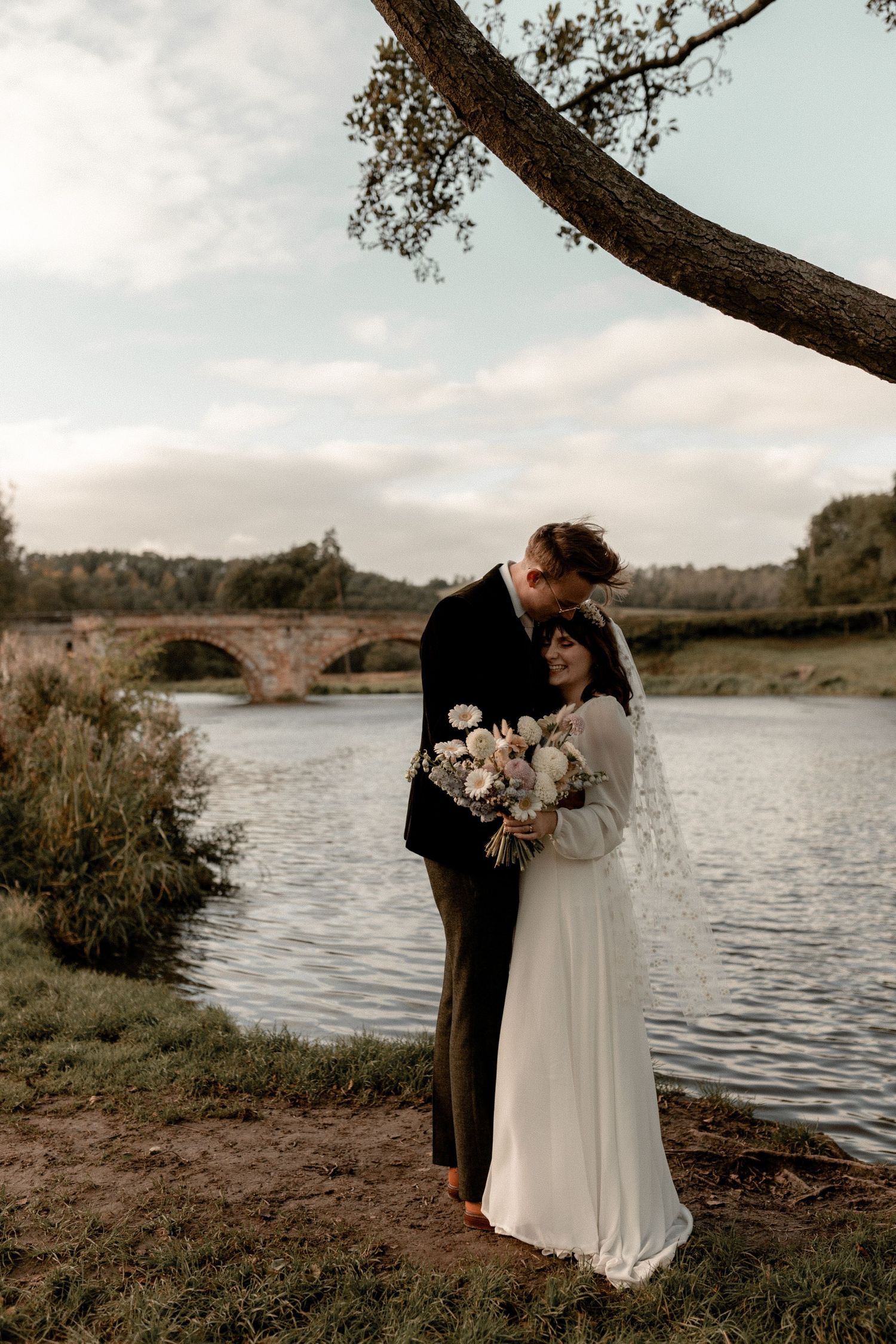 A romantic riverside wedding portrait under an overhanging tree branch.