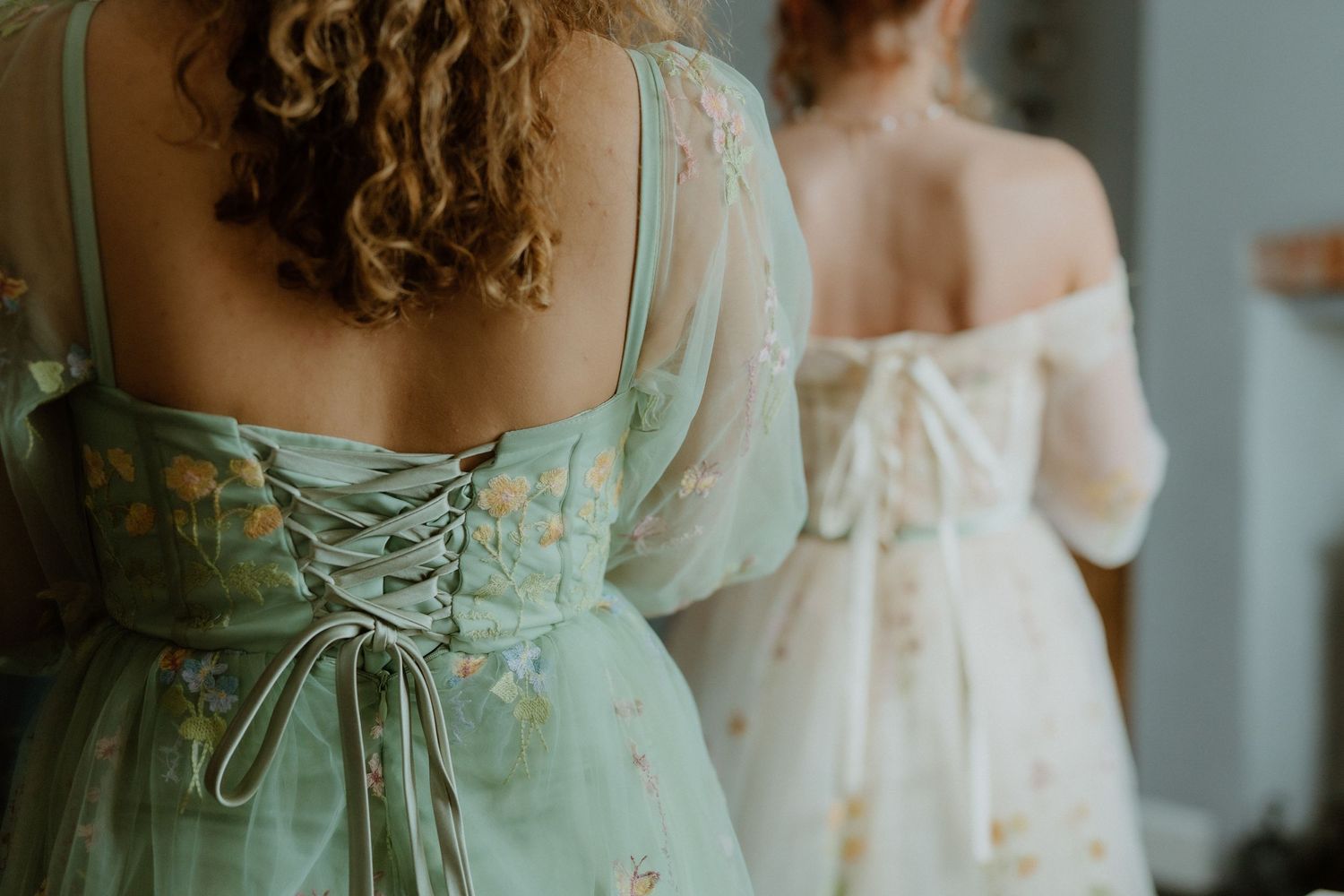 Two elegant vintage-style dresses shown from behind with corset lace detailing in mint green and cream colors.