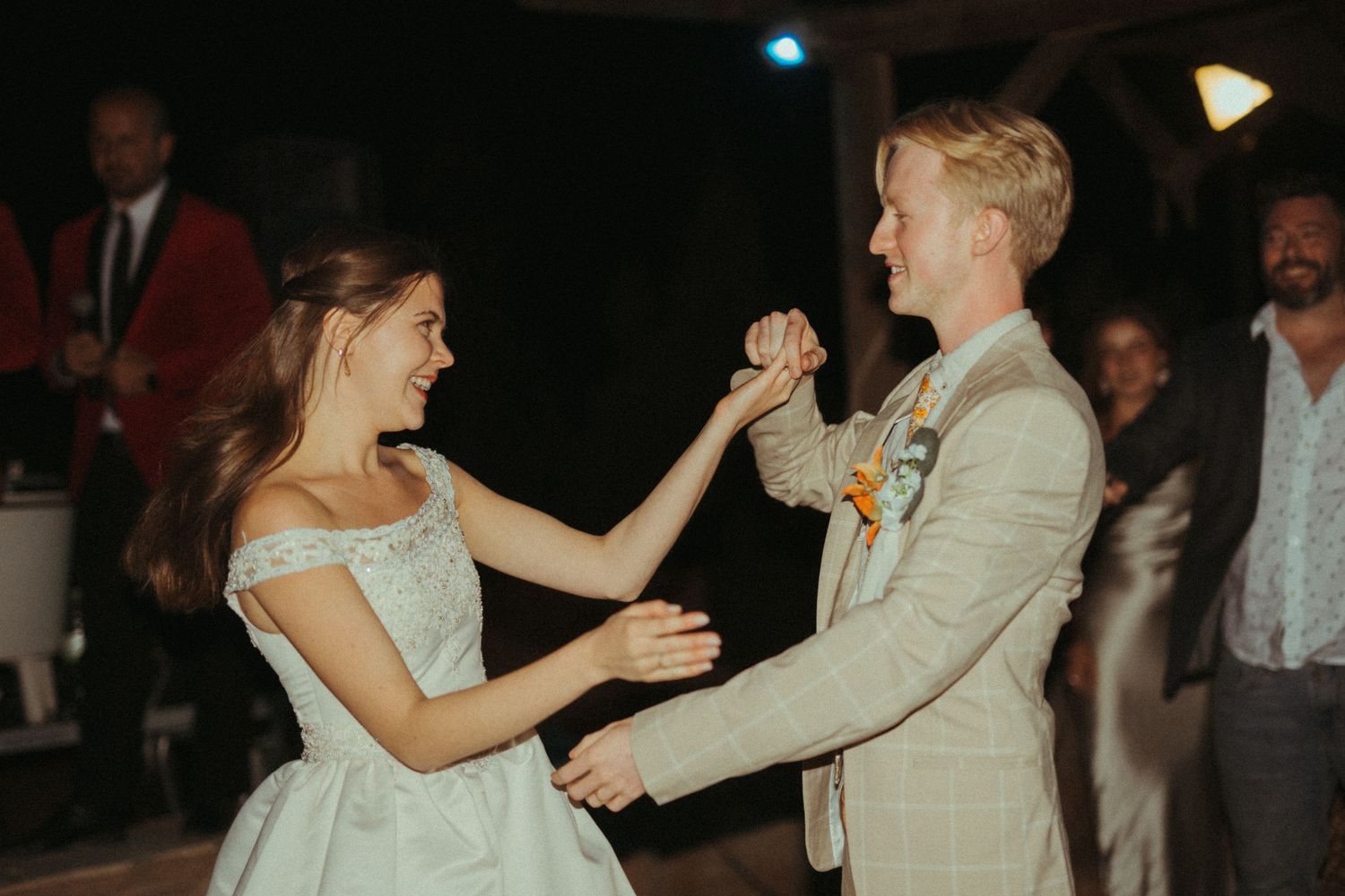 Smiling bride and groom dancing together joyfully at outdoor wedding reception at night.