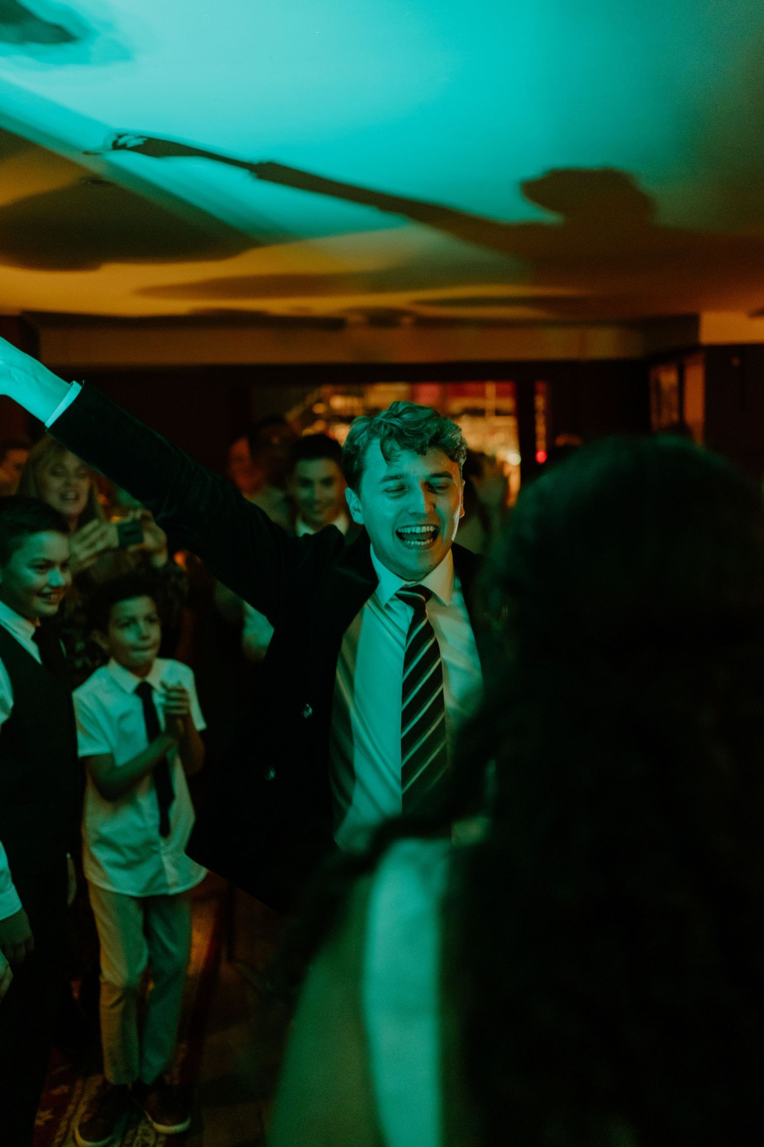 Excited wedding guest raising his arm on the dance floor at a vibrant reception.