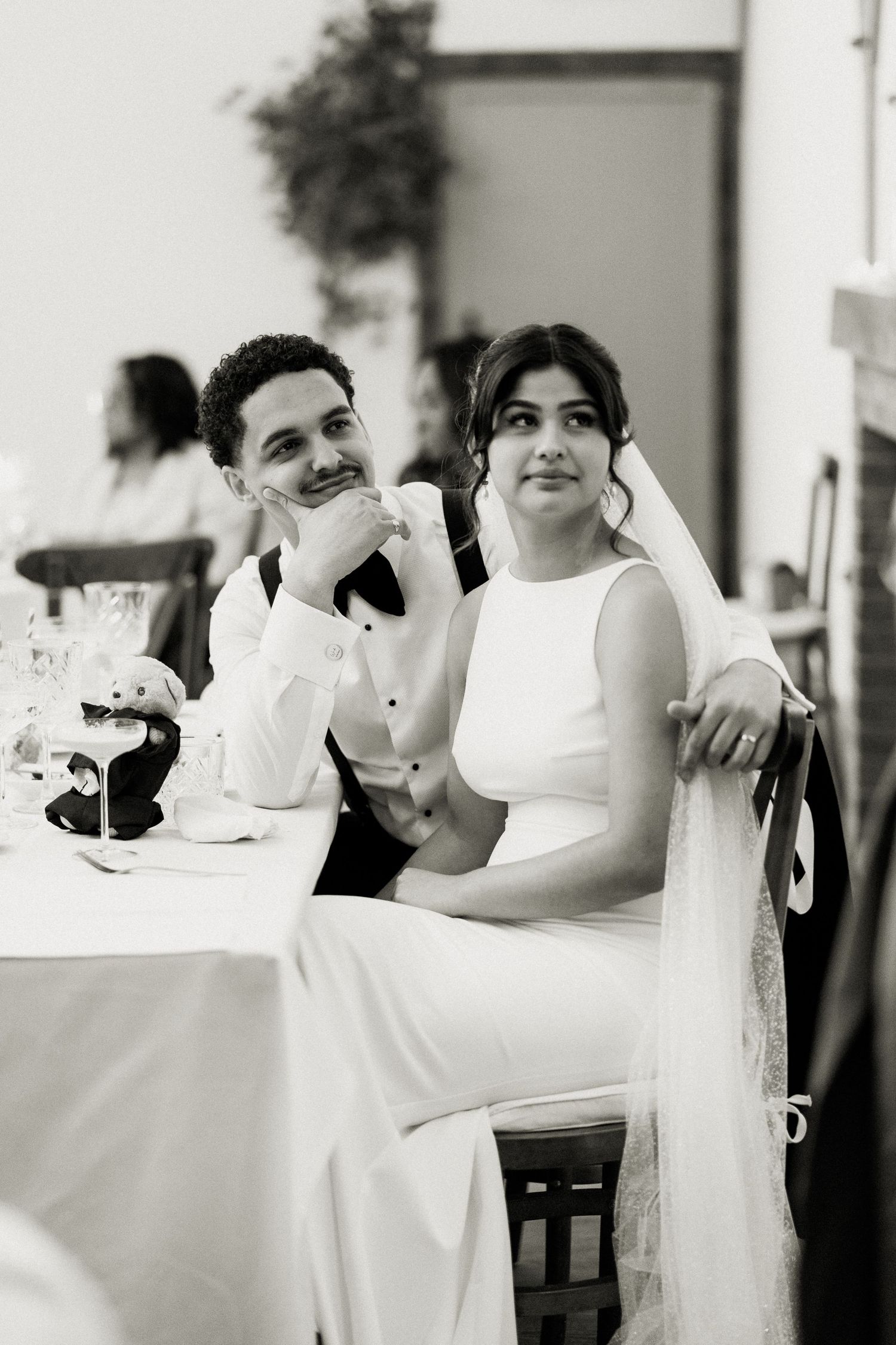 Black and white portrait of bride and groom seated together listening to wedding speeches.