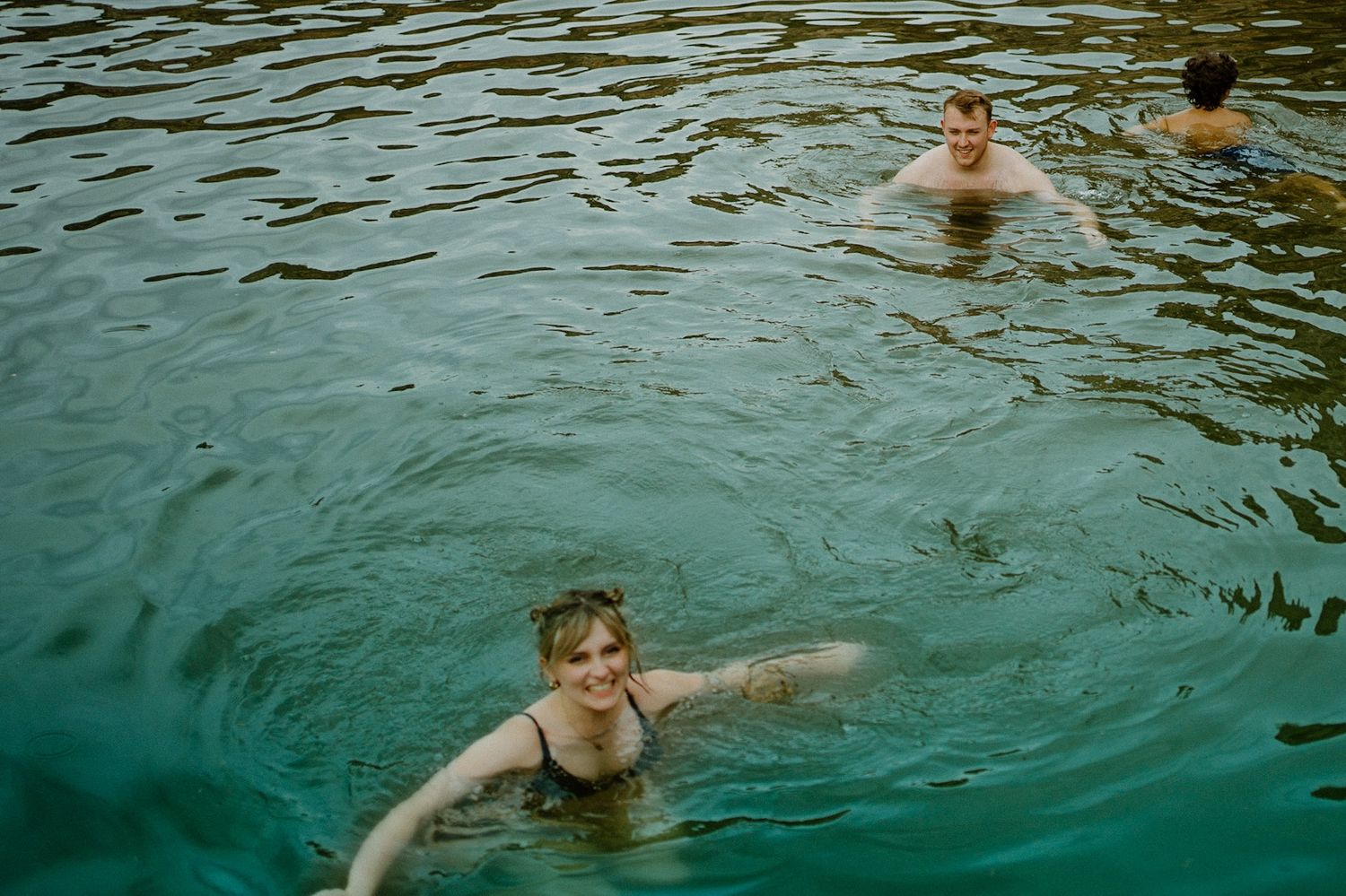 Someone swimming in turquoise rippling water on a sunny day, creating concentric circles in the natural pool.