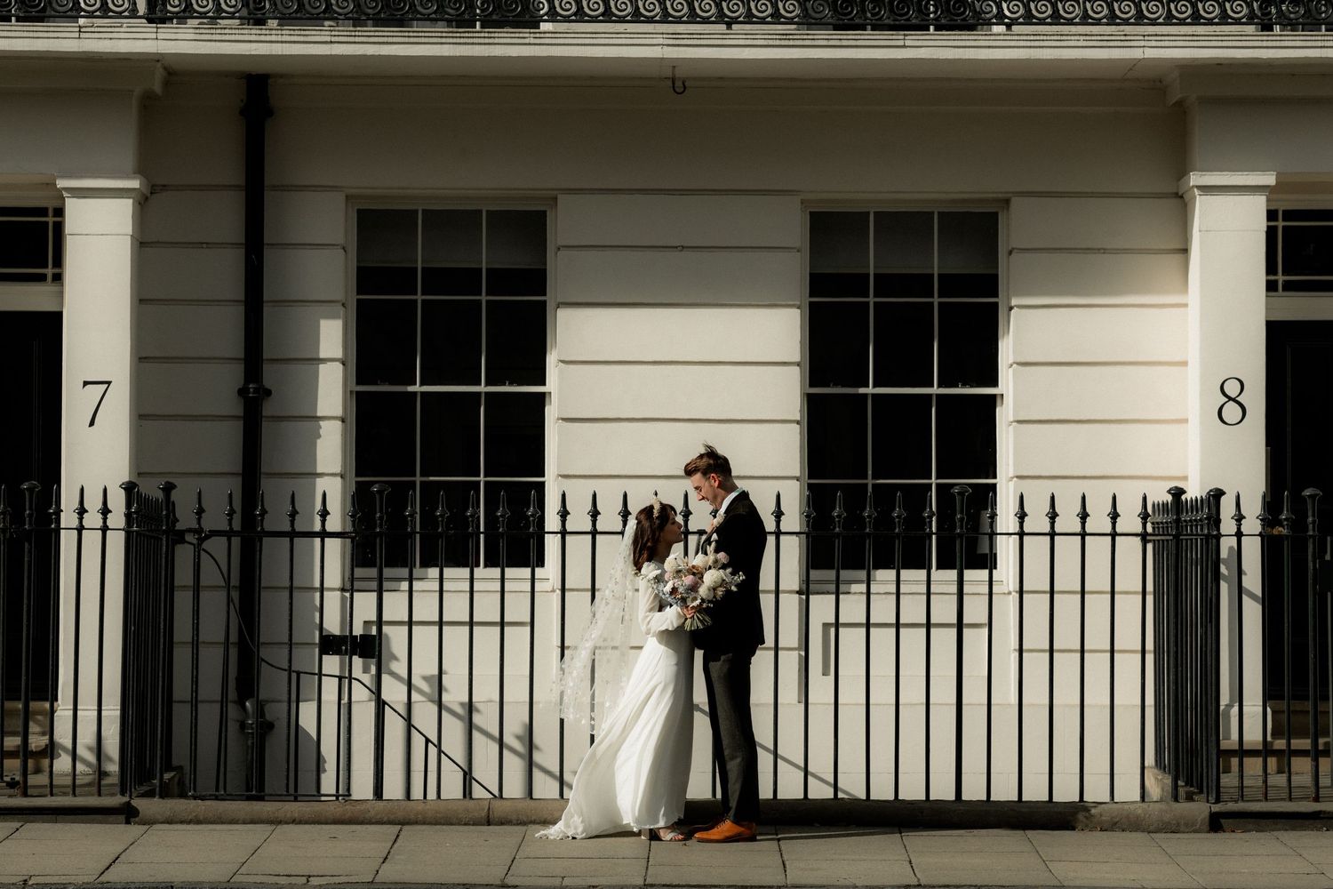 A romantic wedding moment captured against a classic white Georgian building with black railings.
