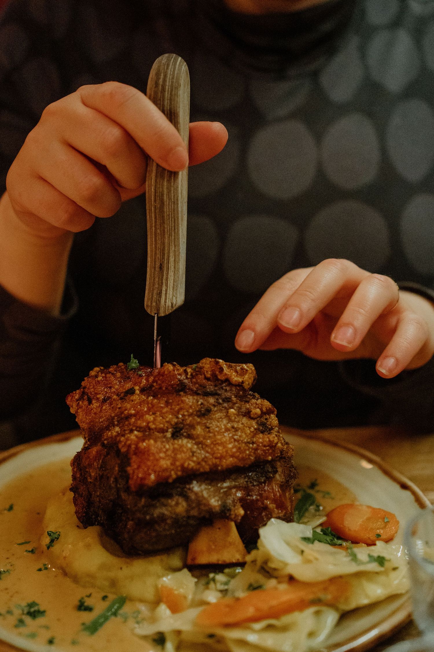 Close-up of a towering burger being held together with a knife on a plate with sauce.