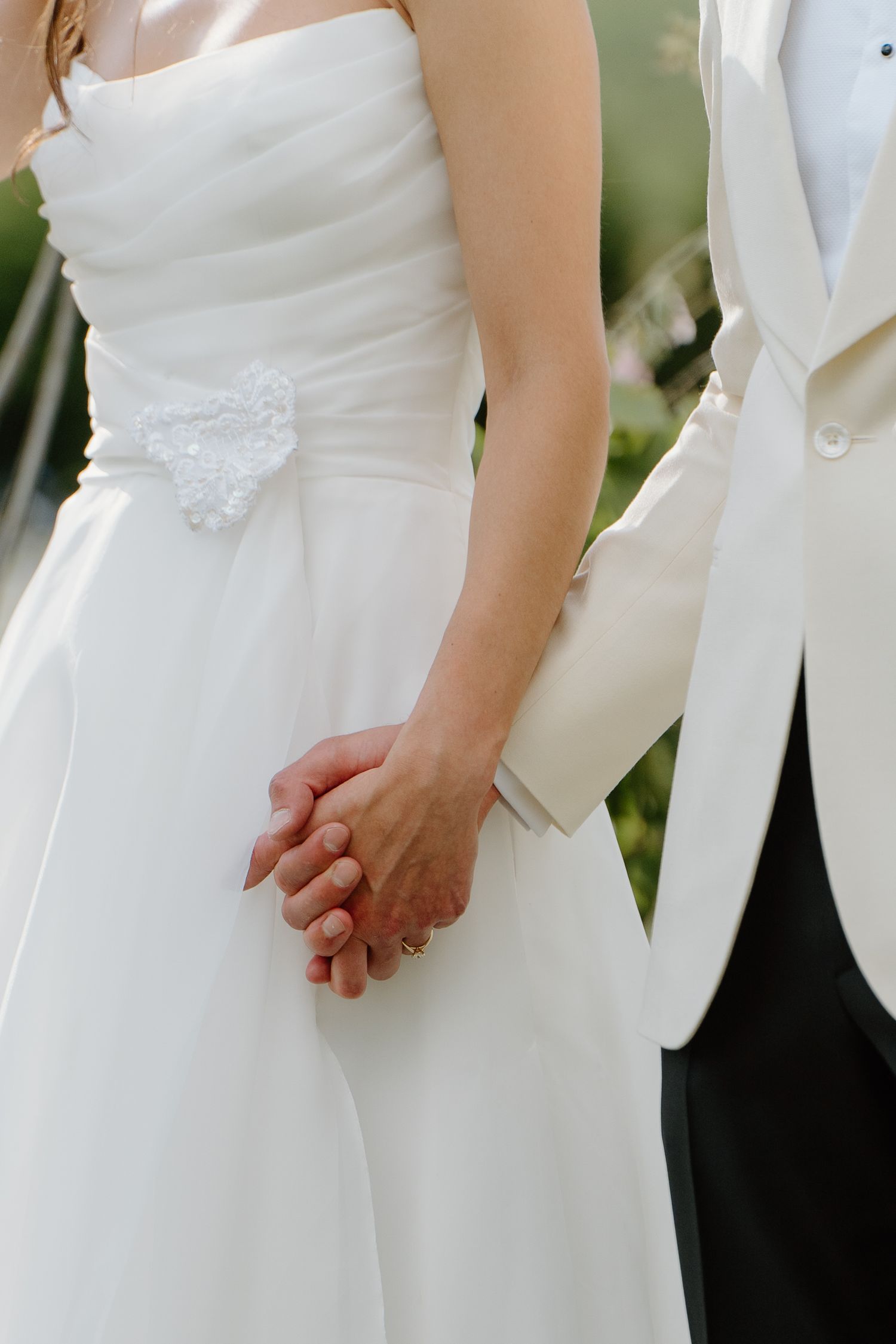 Bride and groom holding hands at wedding ceremony, bride in white strapless gown with lace detail.