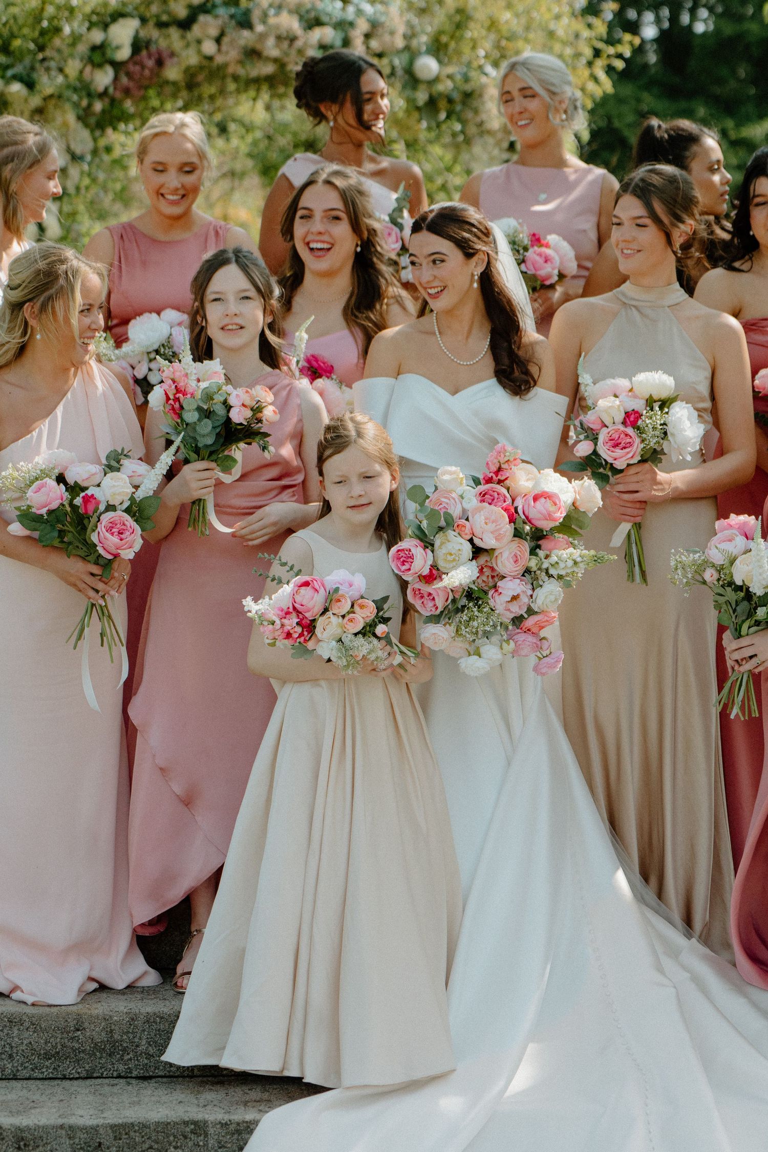 Bride with bridesmaids in pink and champagne dresses holding lush pink and white floral bouquets.
