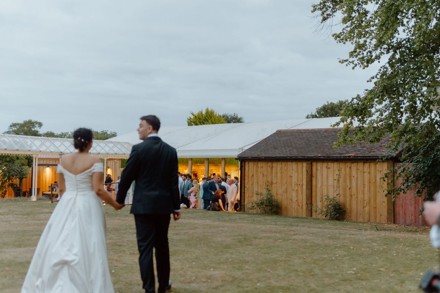 Bride and groom walk hand in hand toward their wedding reception venue at golden hour.