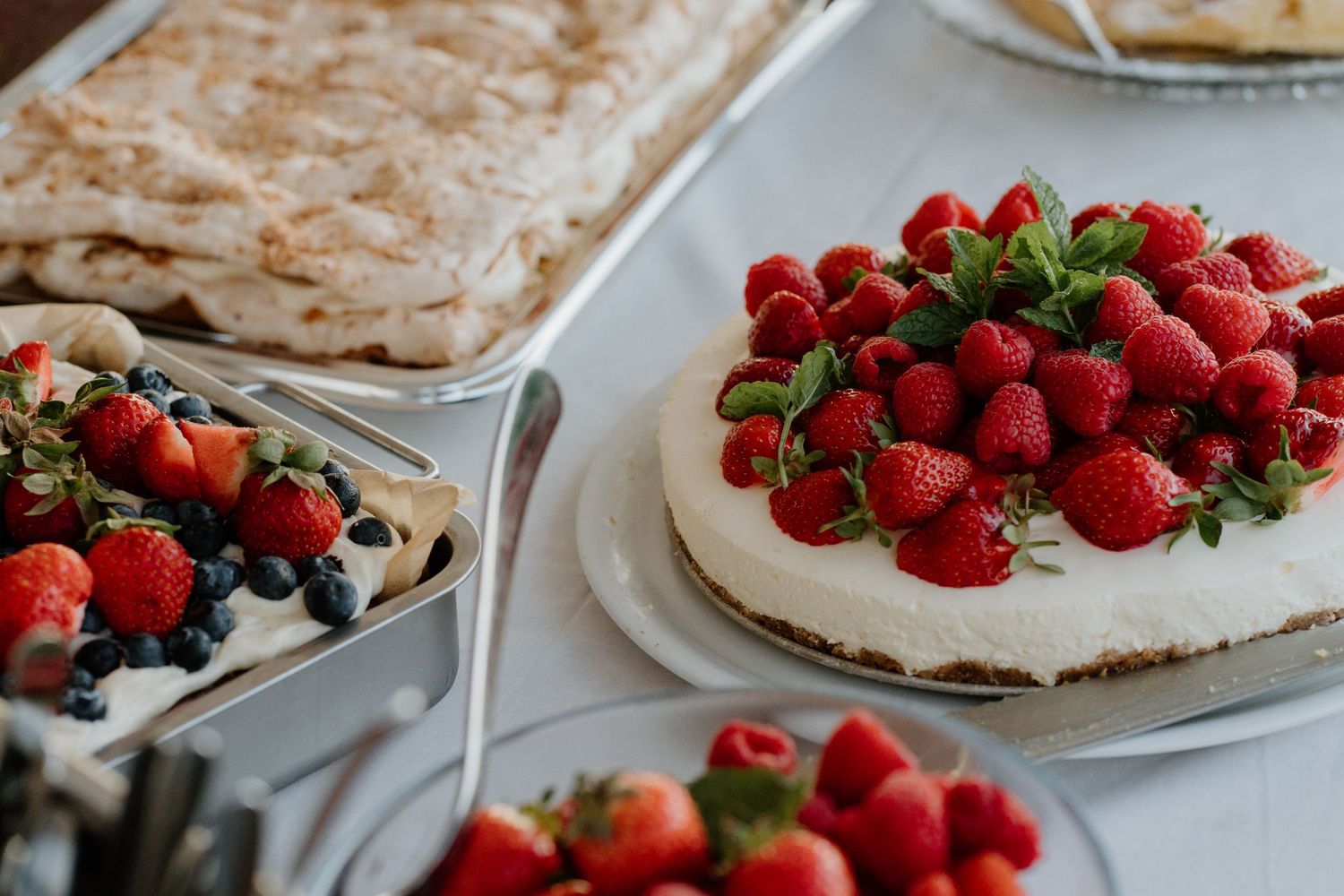 Elegant wedding dessert table featuring cream cake topped with fresh strawberries, raspberries, and blueberries.