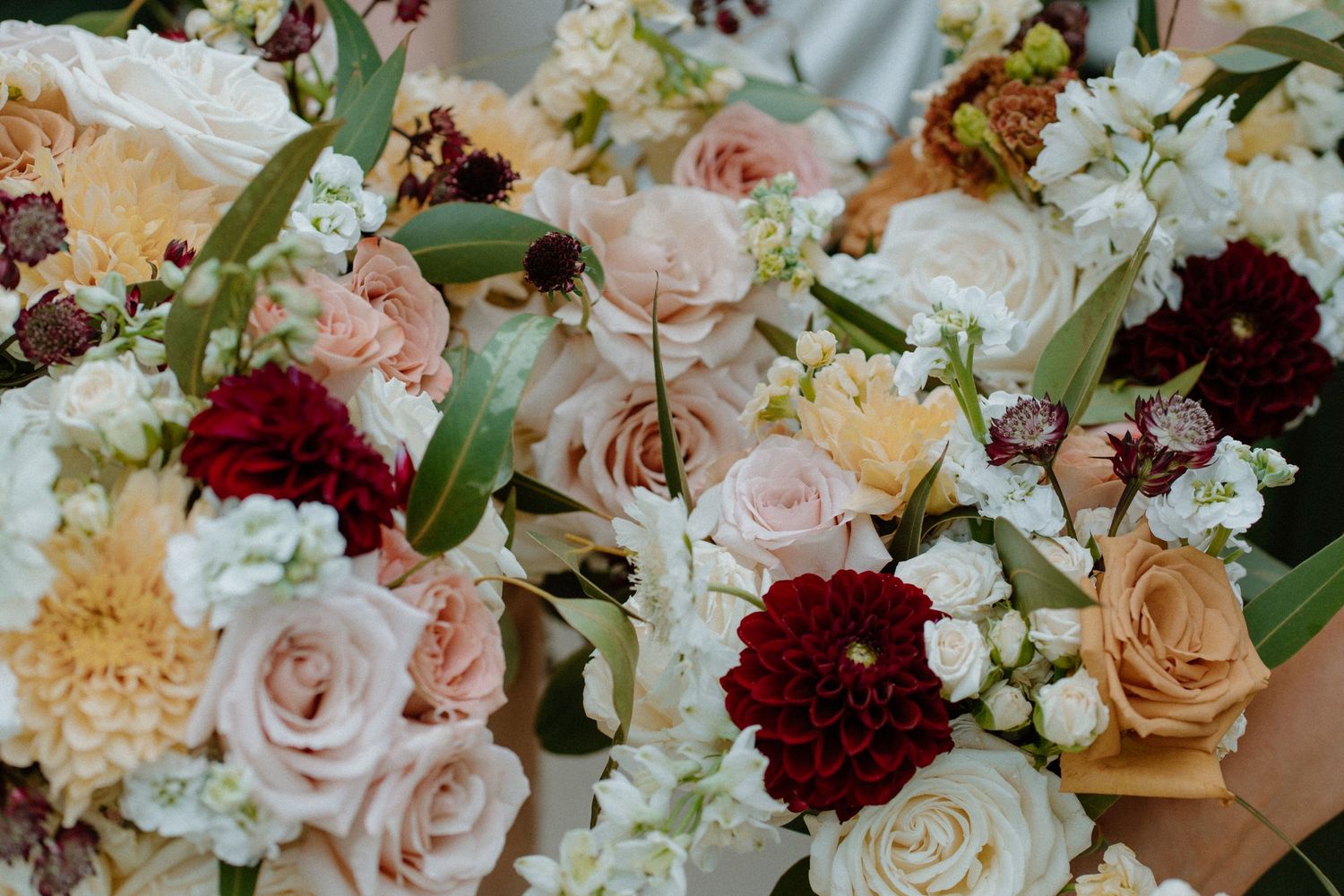 Elegant wedding bouquet arrangement featuring red dahlias, blush roses, and white flowers with greenery.