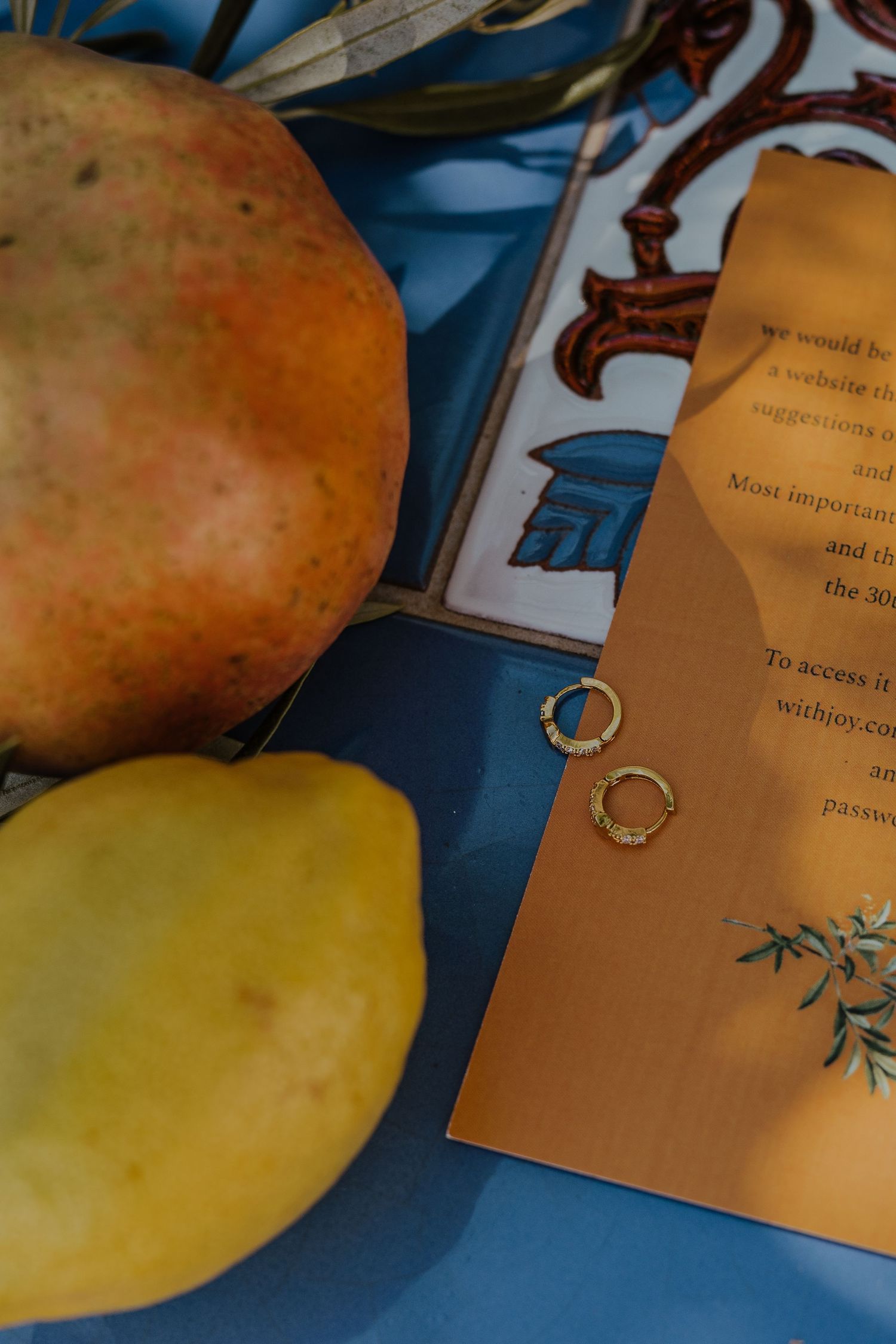 Gold wedding rings resting on an orange wedding invitation card surrounded by ripe pears on blue.