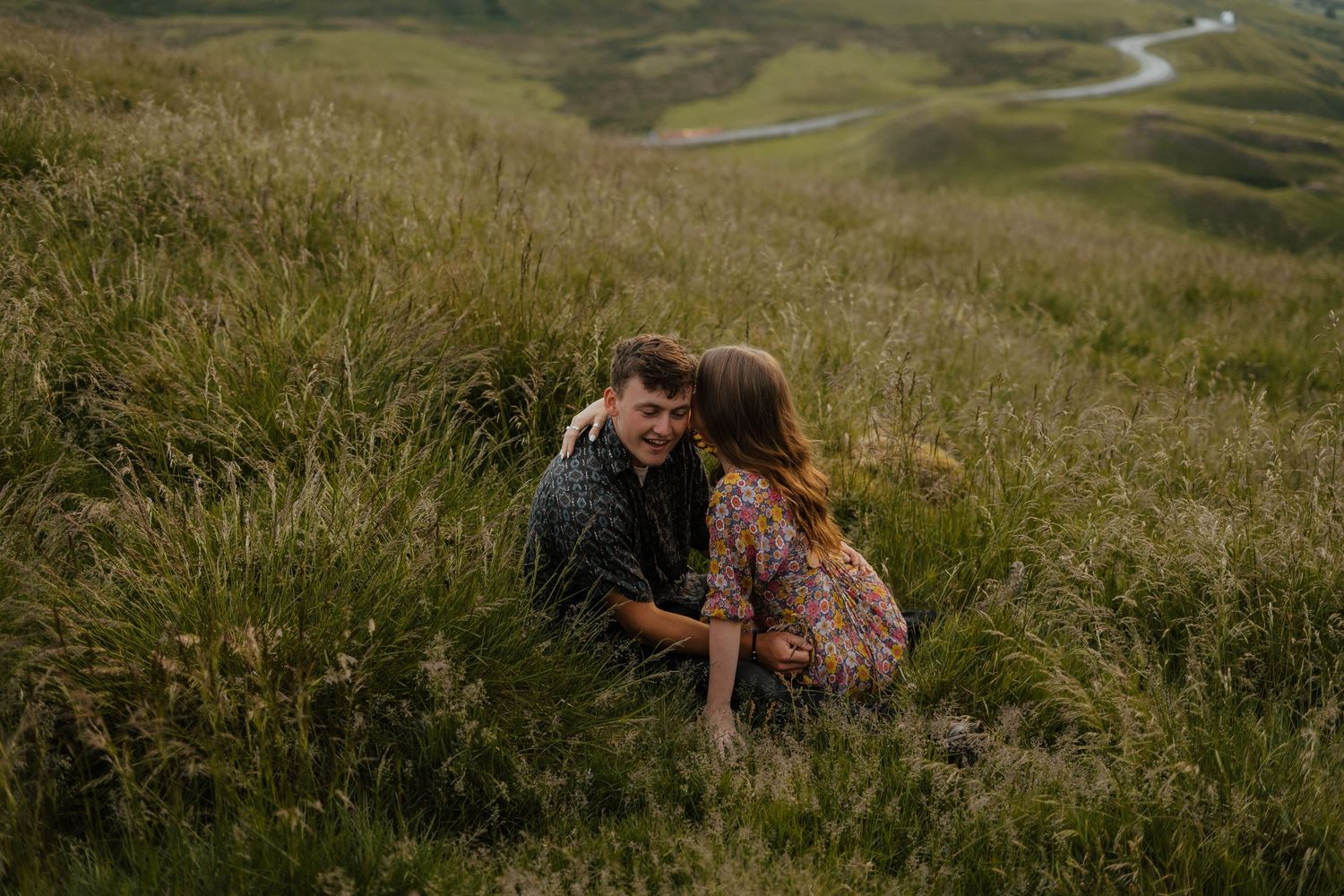 Couple sharing a tender moment sitting close together in a lush green grassy hillside.