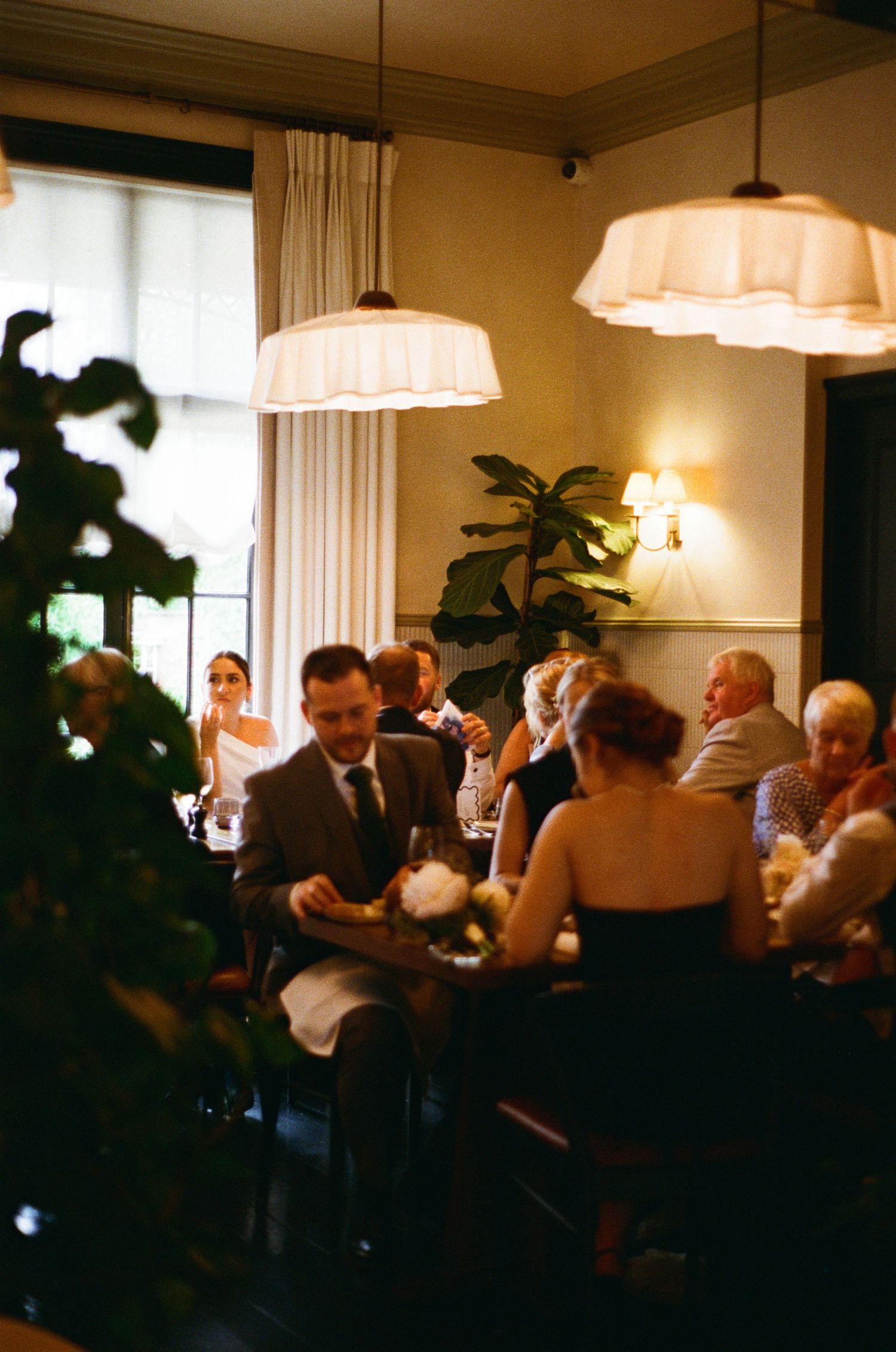 Wedding guests seated at dinner tables under warm pendant lights in cozy restaurant.