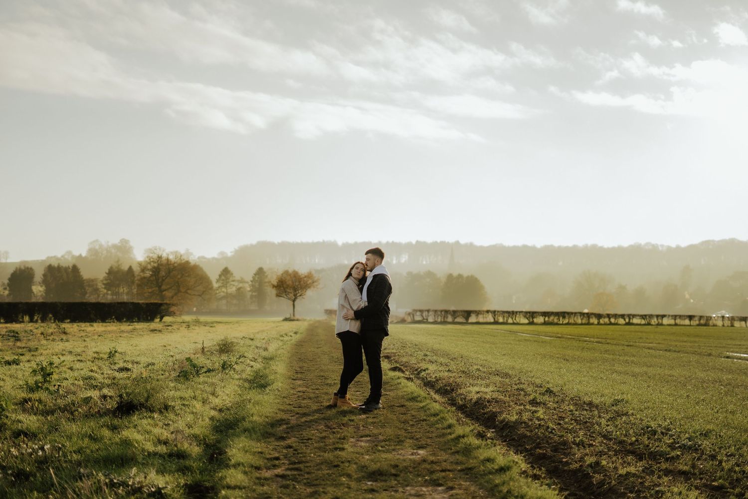 Couple embracing romantically at golden hour in a misty open countryside field.