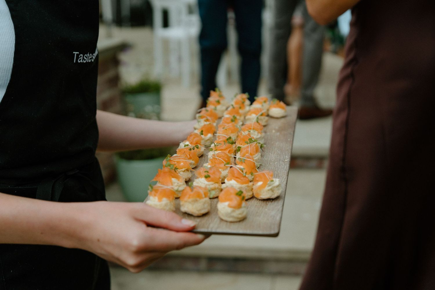 Catering staff presents elegant wooden board of smoked salmon canapes at wedding reception.