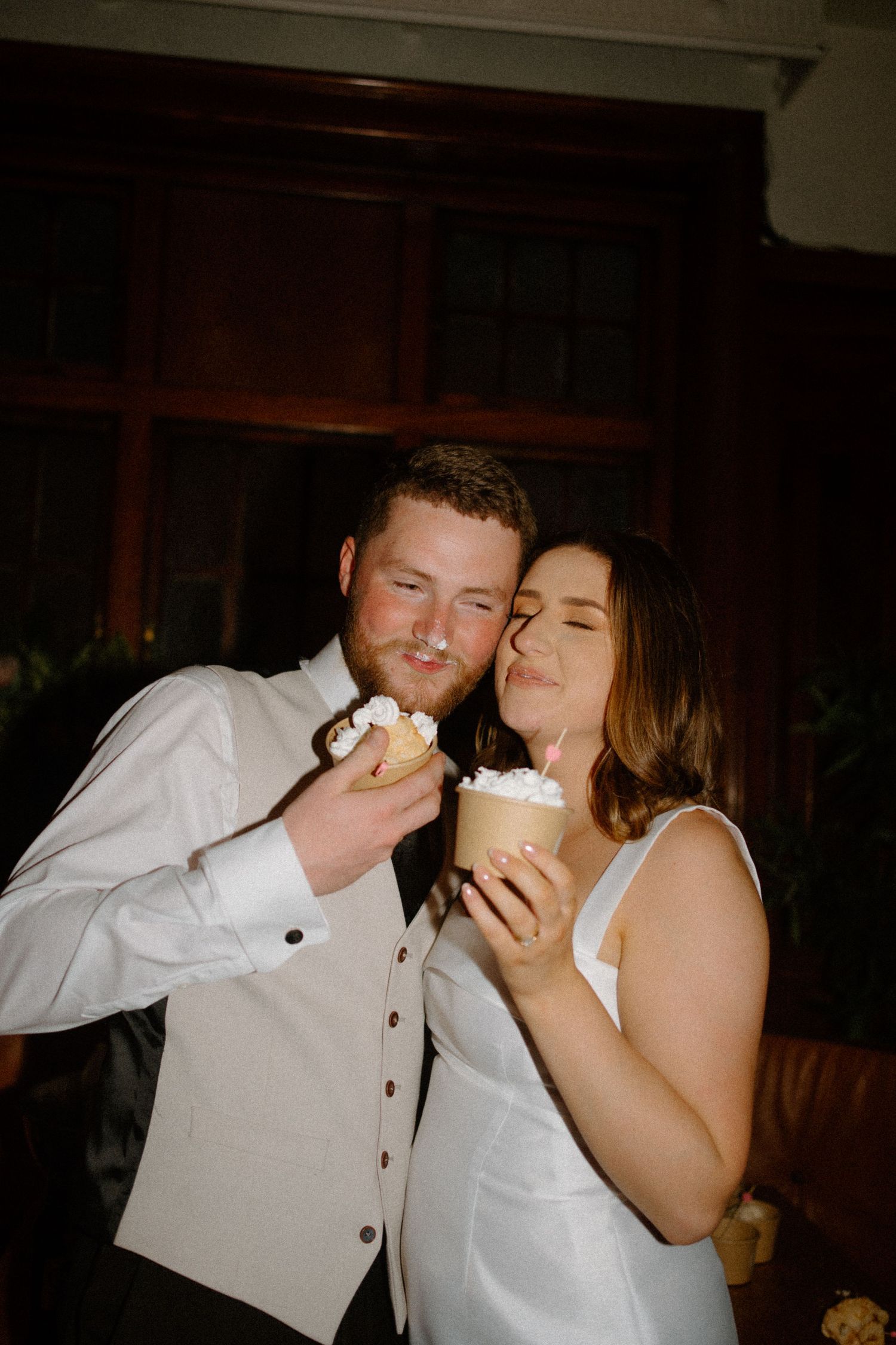 A couple in wedding attire share a sweet moment while enjoying cupcakes at their reception.