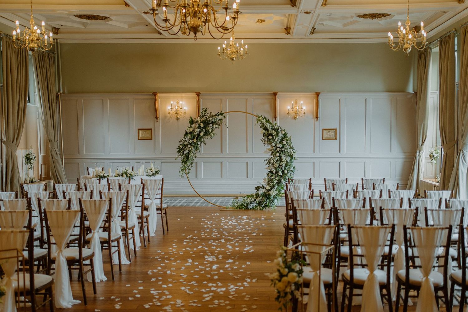 Elegant wedding ceremony room with floral arch, petal aisle, chandeliers and chiavari chairs.