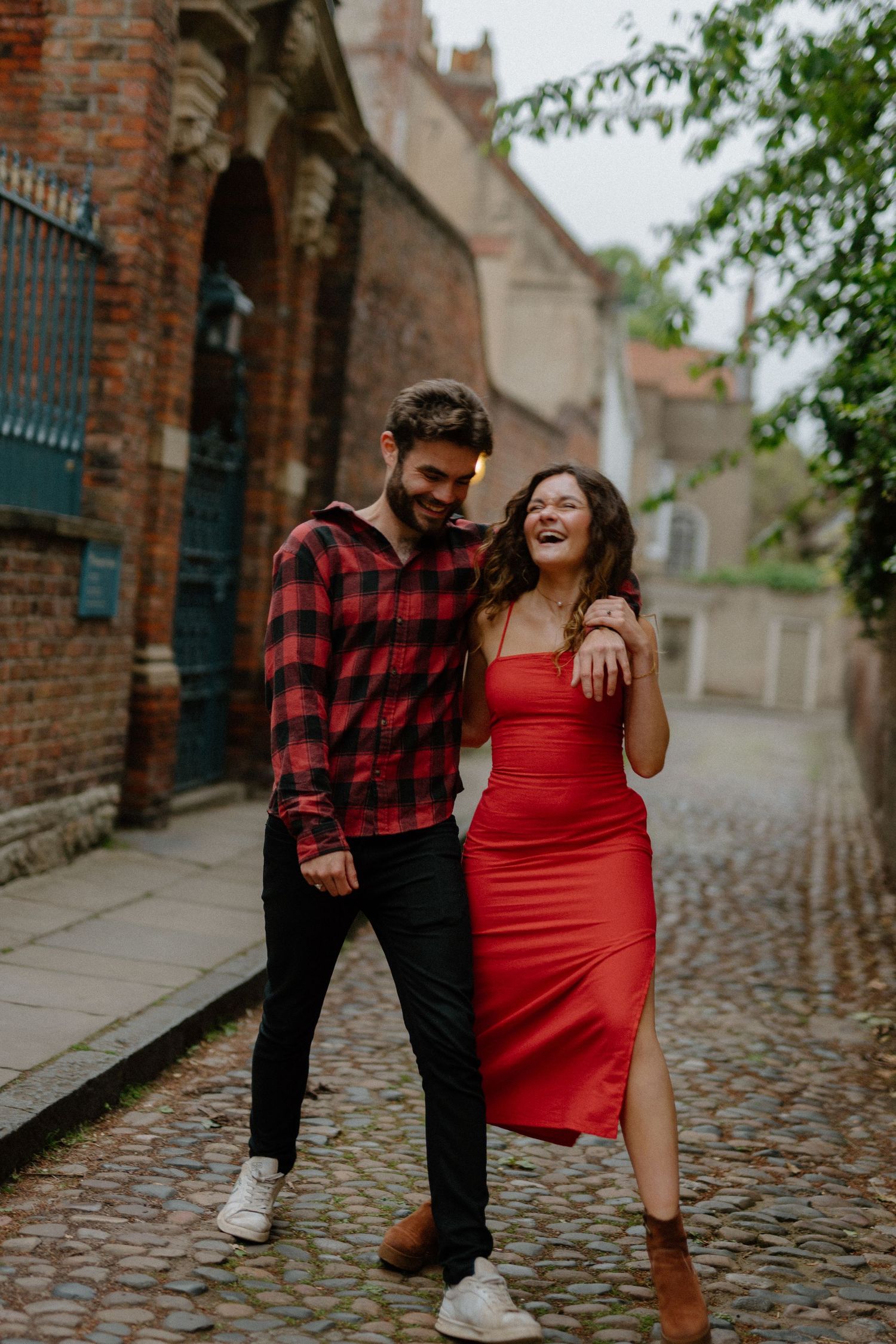 Laughing couple strolling together on a cobblestone street surrounded by old brick buildings.