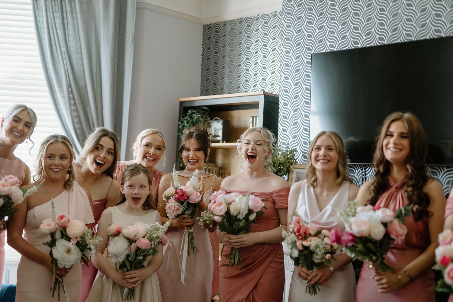 Bridesmaids in pink and champagne dresses laughing and holding bouquets of pink and white flowers.