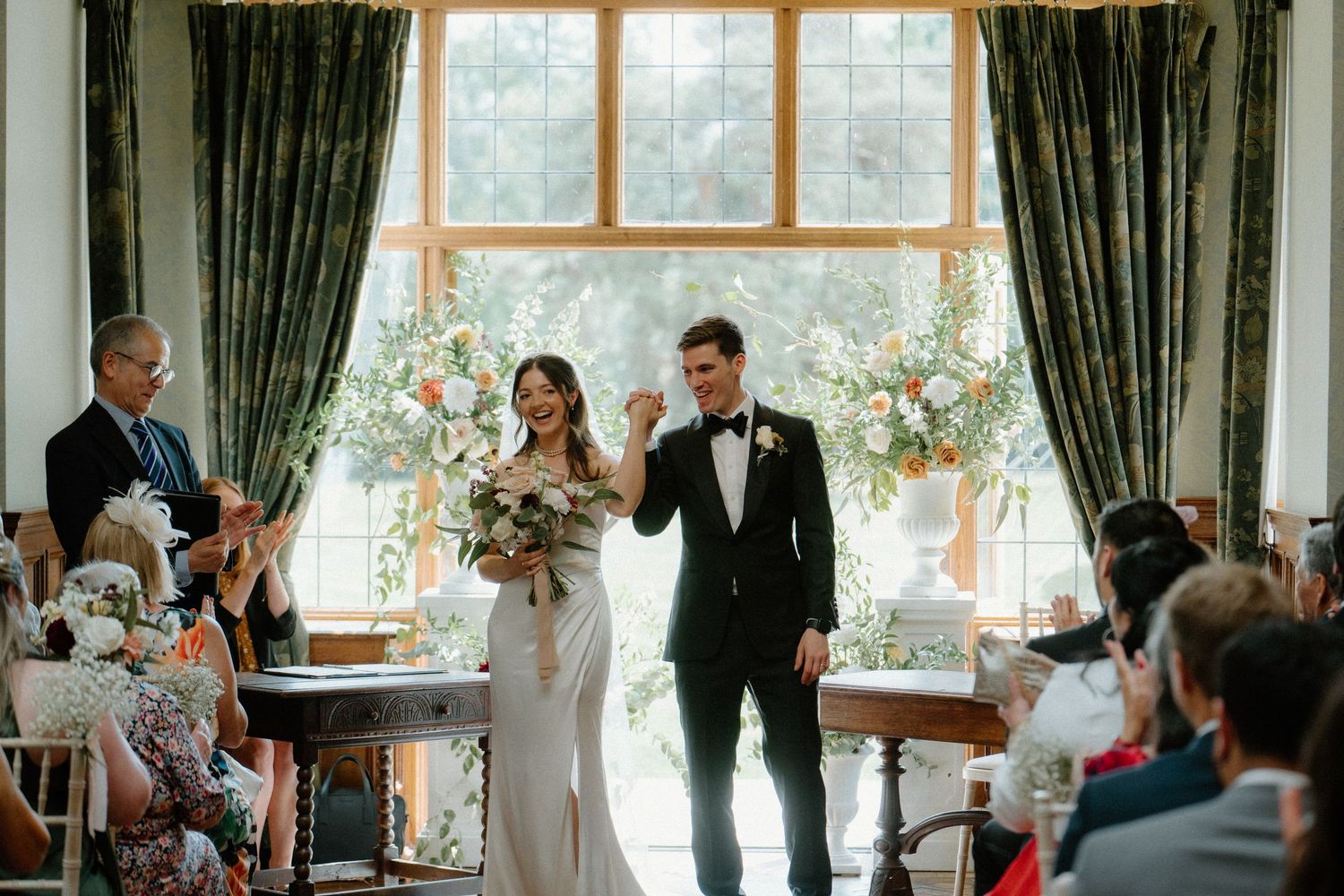 Newlyweds celebrate walking back down aisle as wedding guests applaud in elegant venue.