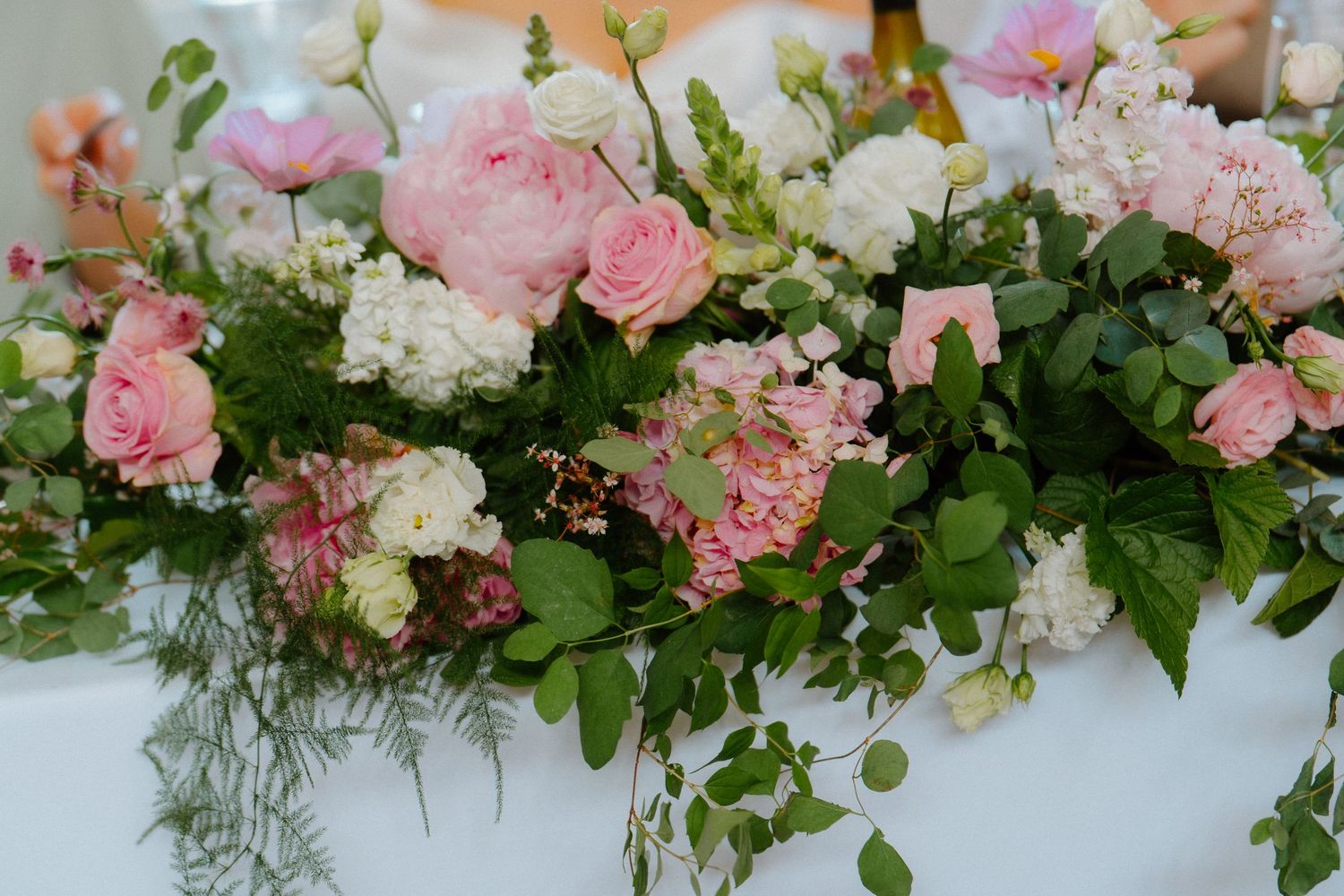 Lush pink and white floral table arrangement with roses and greenery for wedding reception decor.