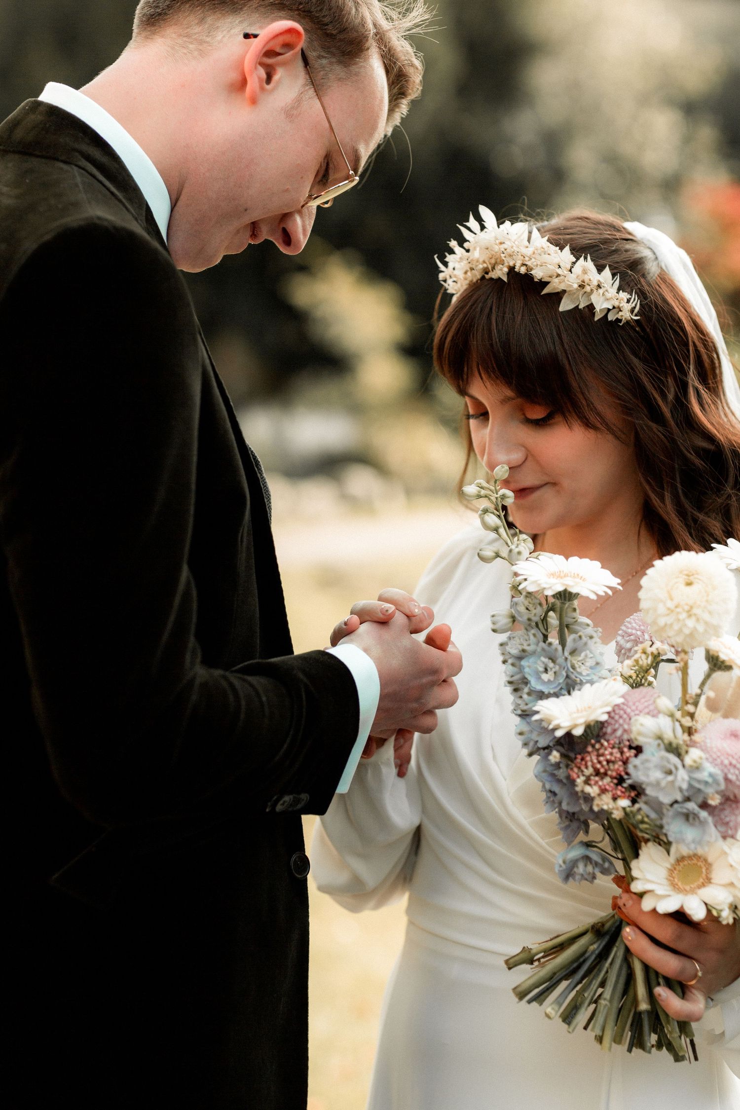 A tender moment between newlyweds as they hold hands, with the bride holding a pastel floral bouquet.