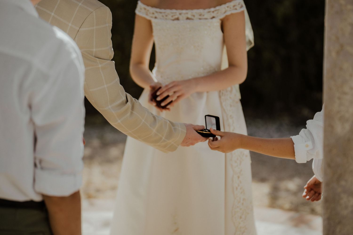 Officiant presenting wedding rings in a box during an outdoor ceremony with bride in white lace dress.
