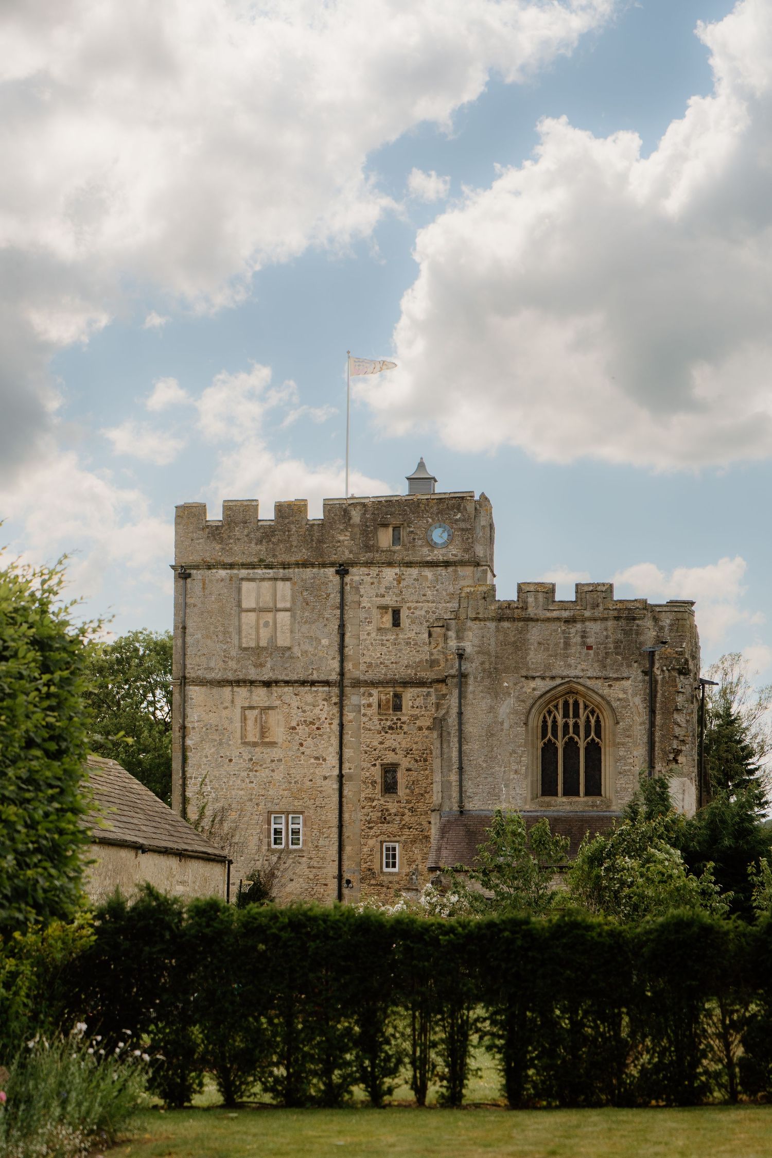 Historic stone castle wedding venue with battlements and Gothic window under a cloudy sky.