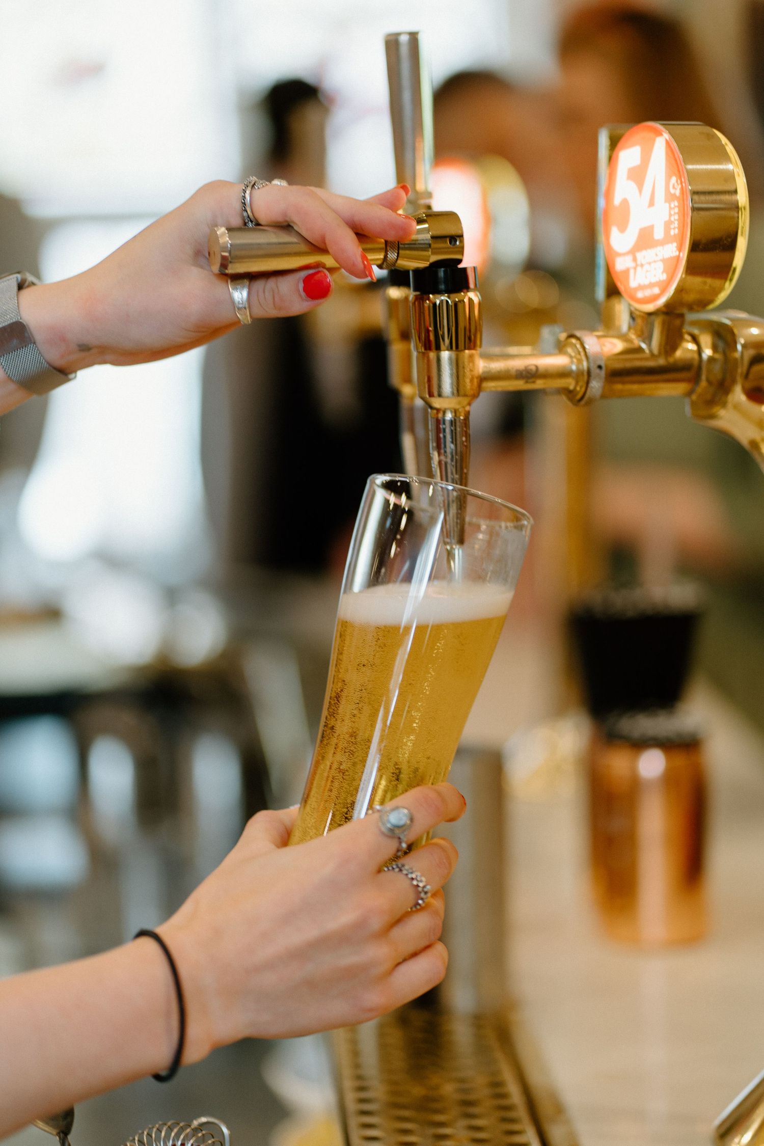Bartender pouring draft beer from golden tap into tall glass at wedding reception bar.