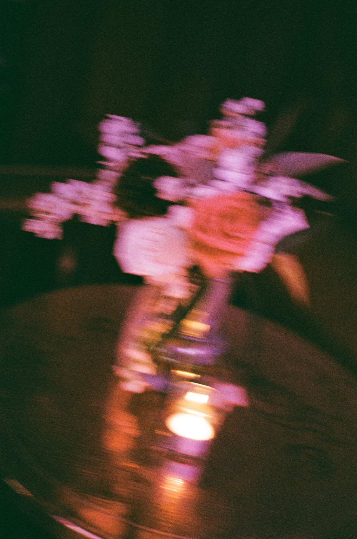 Blurry film photo of pink and white roses in a glass vase with a glowing candle on a dark wooden table.