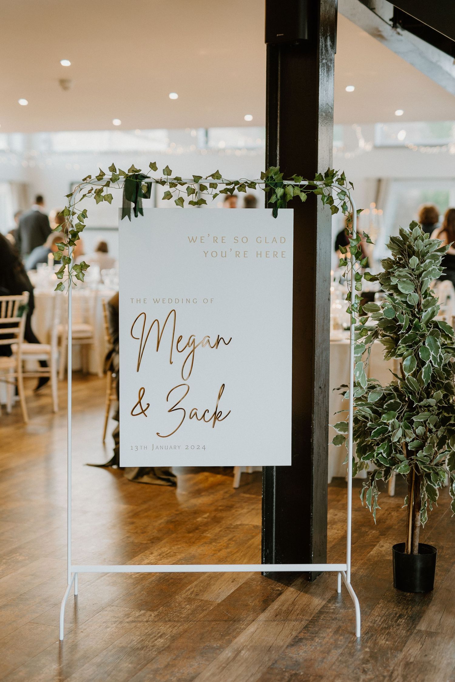 Elegant wedding welcome sign for Megan and Zack decorated with greenery on a white easel in a bright reception venue.