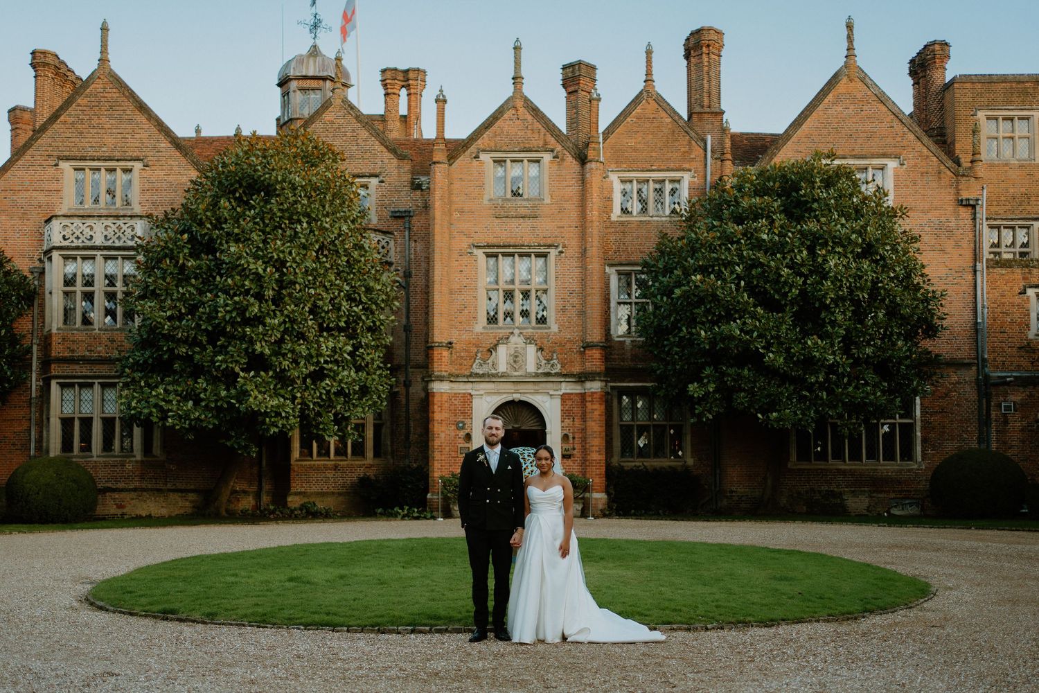 Bride and groom posing in front of a grand red brick English manor house on their wedding day.