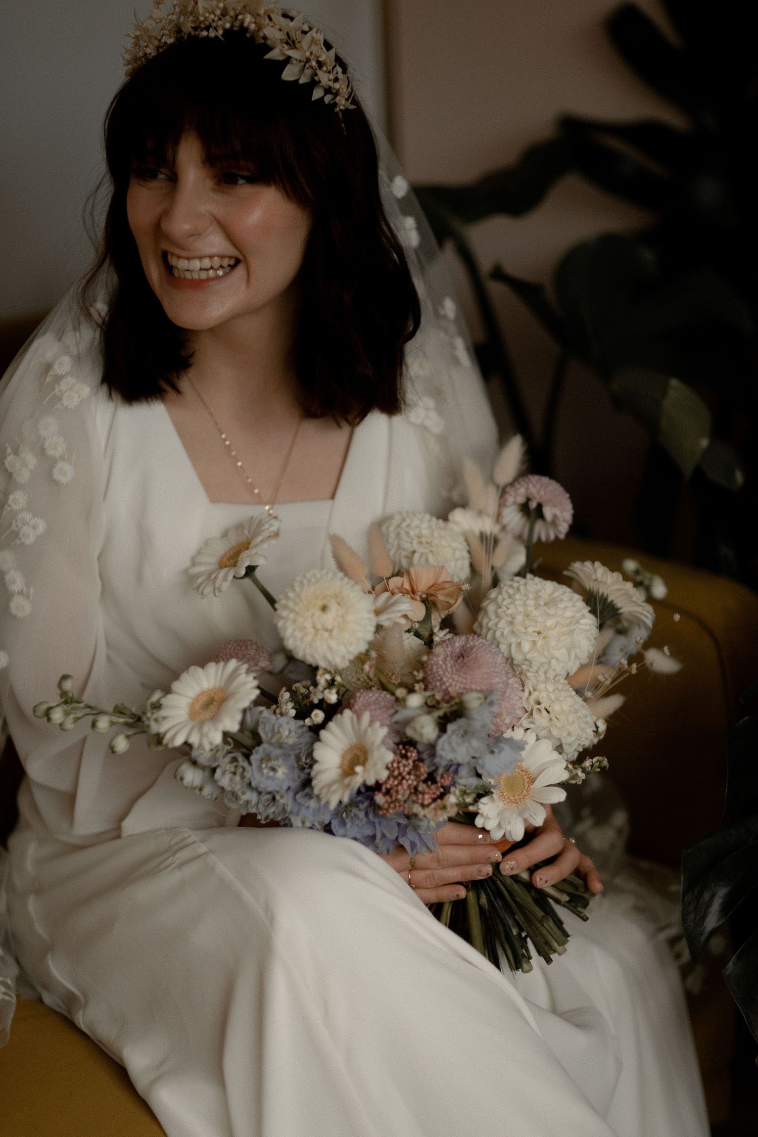 A bride in a white dress holding a bouquet of mixed pastel flowers and wearing a crystal headpiece.