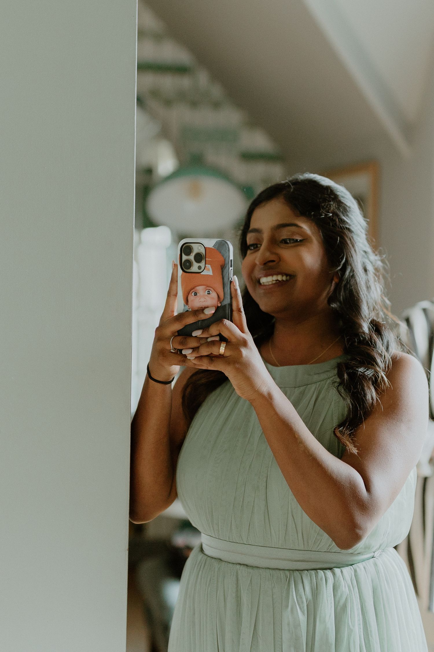 Smiling bridesmaid in mint green dress taking a selfie with a phone in a colorful case.