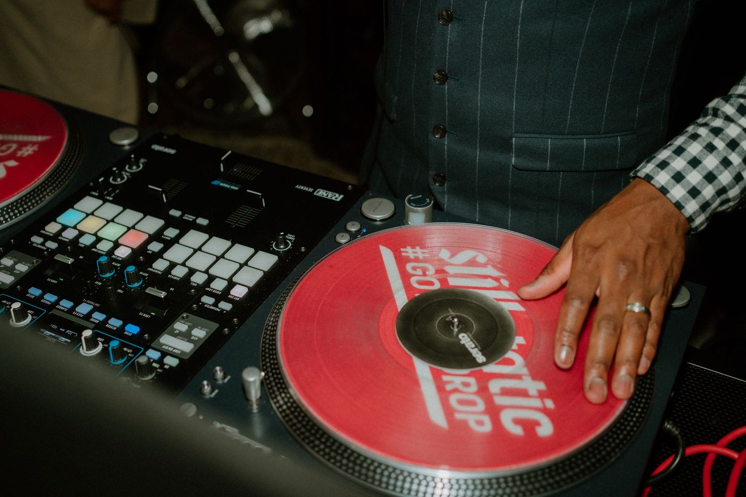 A DJ's hand rests on a red vinyl record on a turntable beside a music production controller.
