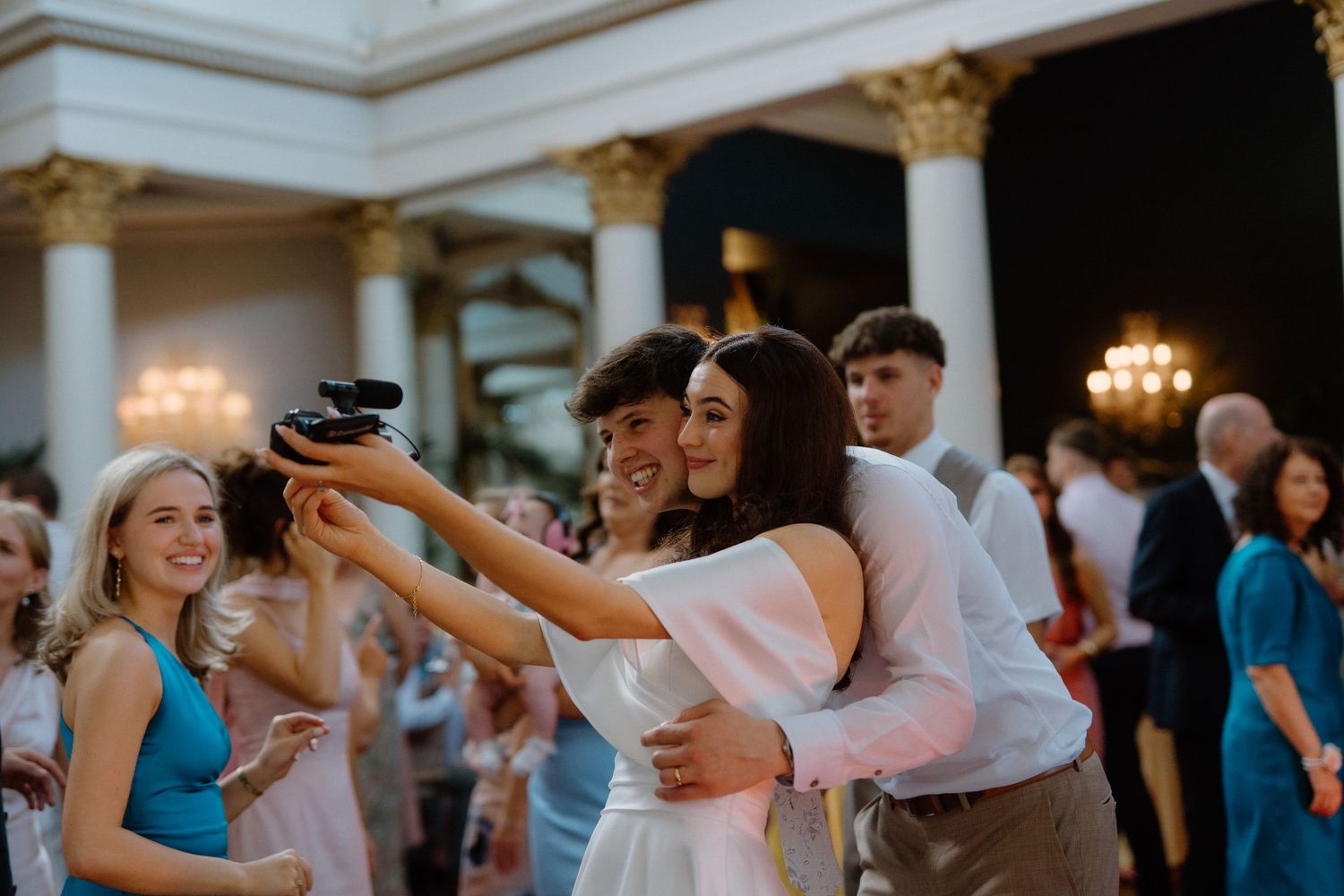 Bride and groom taking a selfie together on the dance floor surrounded by wedding guests.