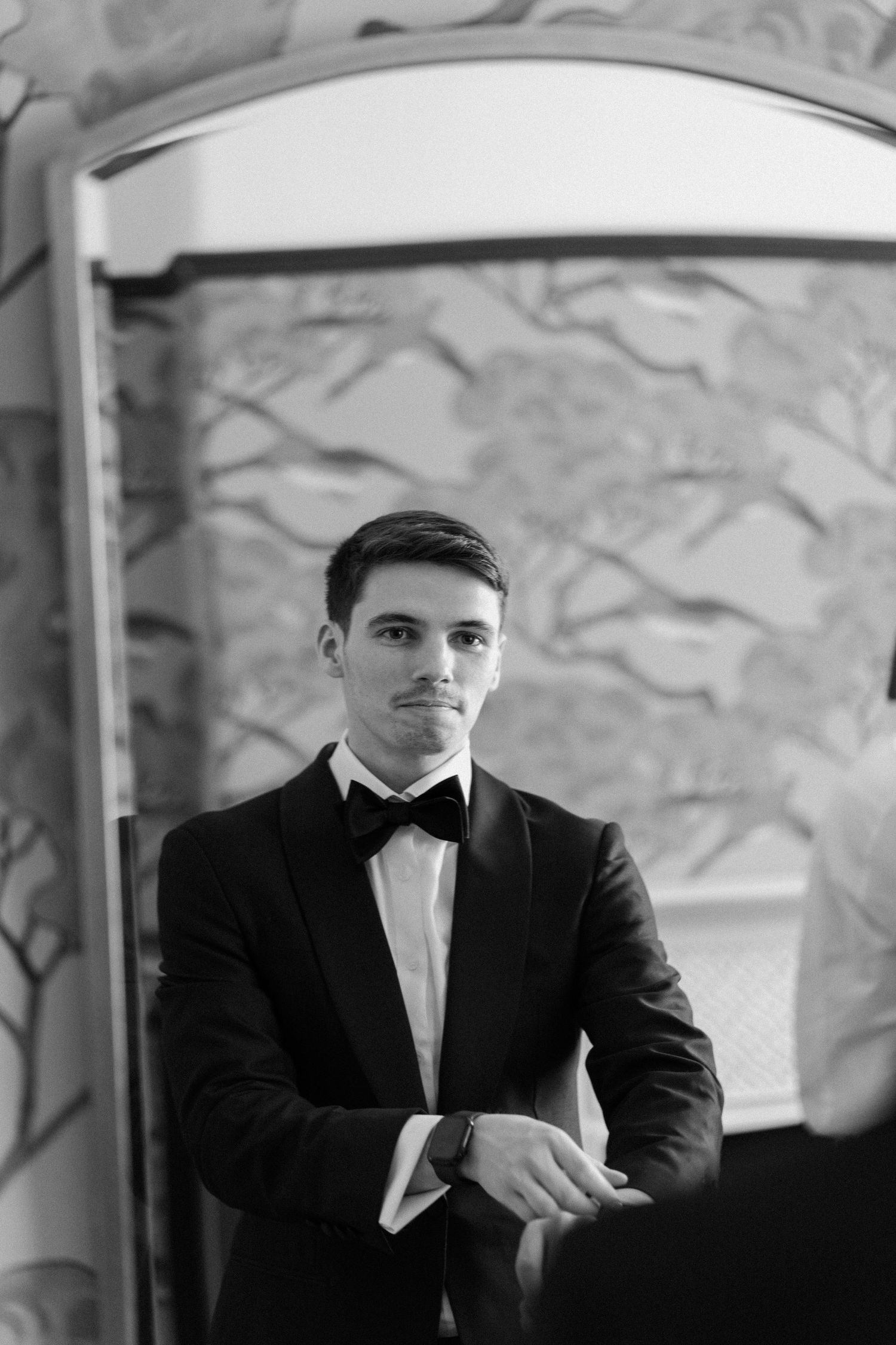 Black and white portrait of handsome groom in black tuxedo and bow tie adjusting cufflinks.