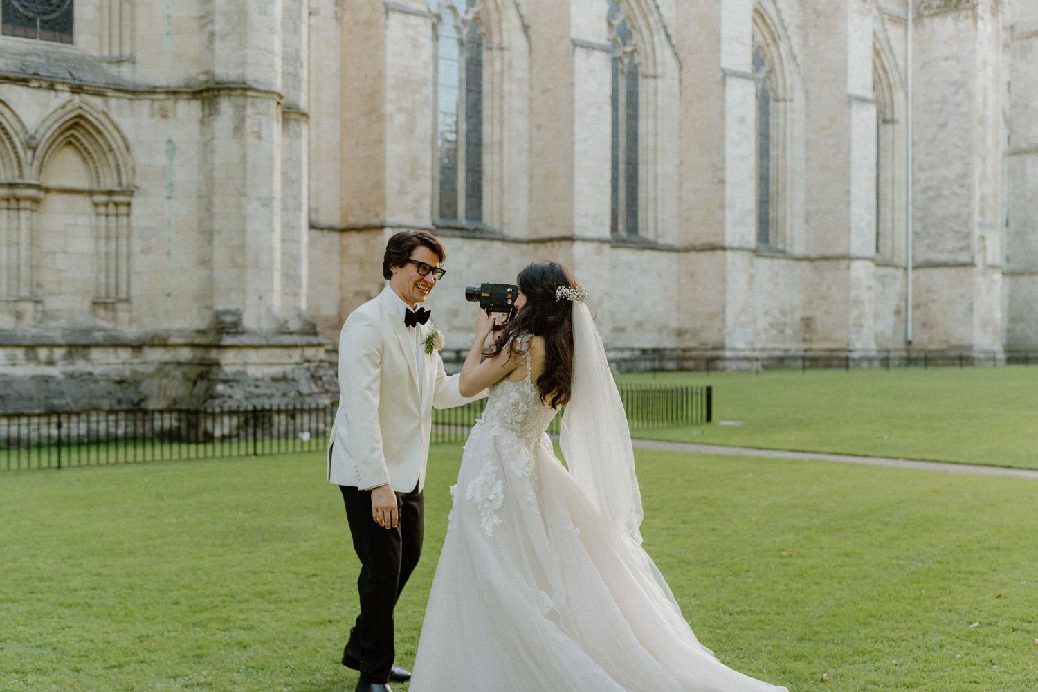 Bride and groom sharing tender moment outside historic Gothic stone cathedral in elegant wedding attire.