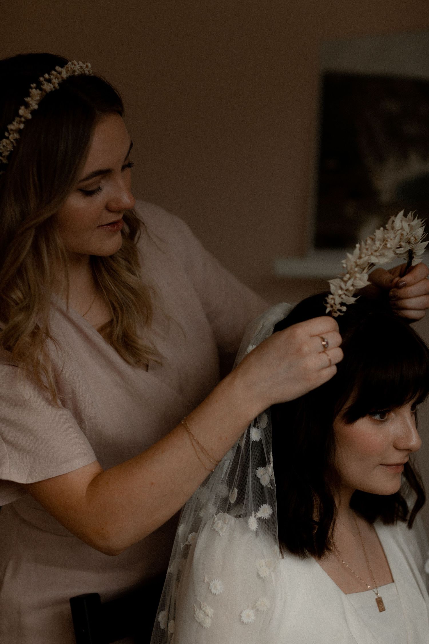 A stylist arranges a delicate floral headpiece on a person wearing white.
