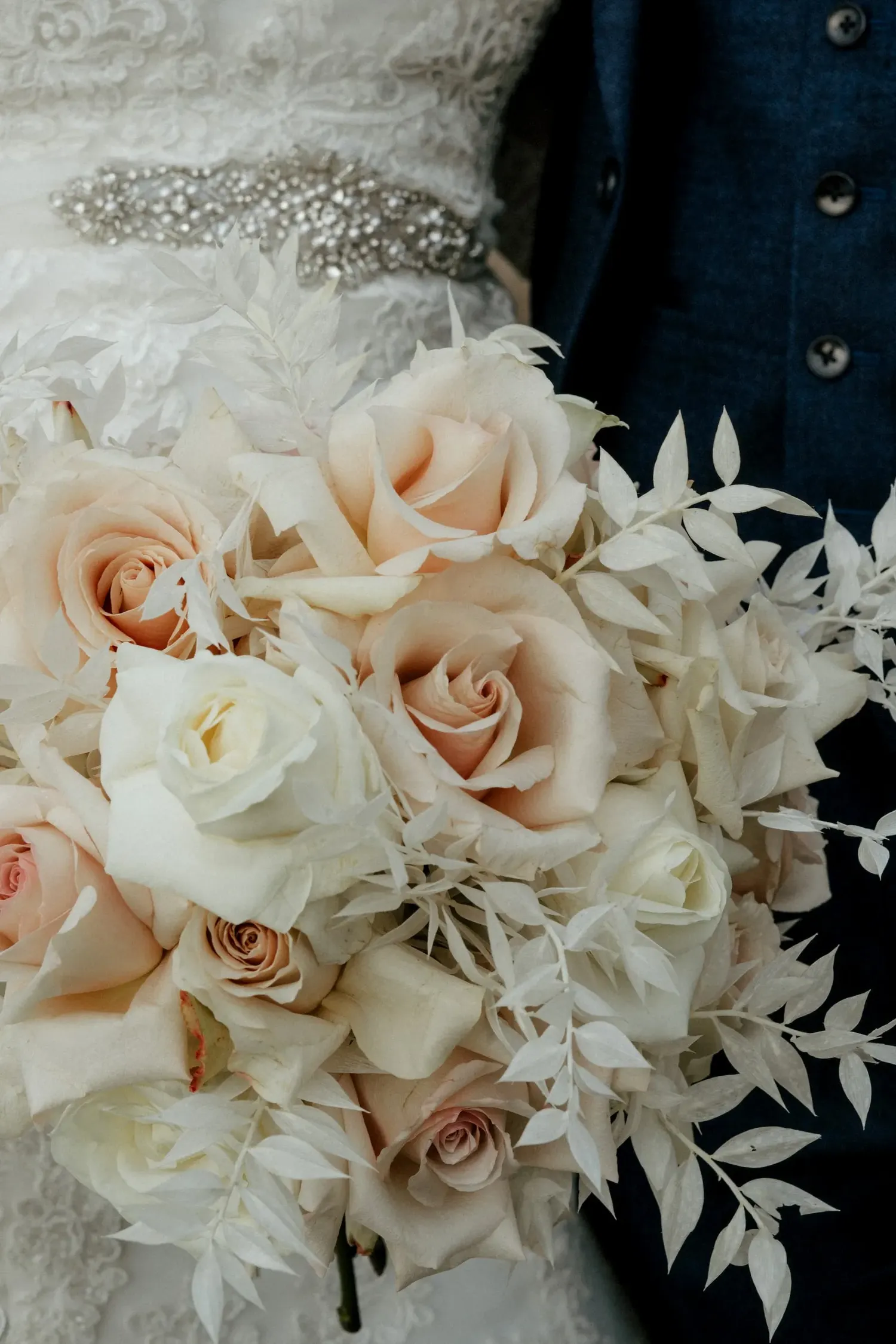 Close-up of elegant blush and white rose wedding bouquet with delicate foliage.