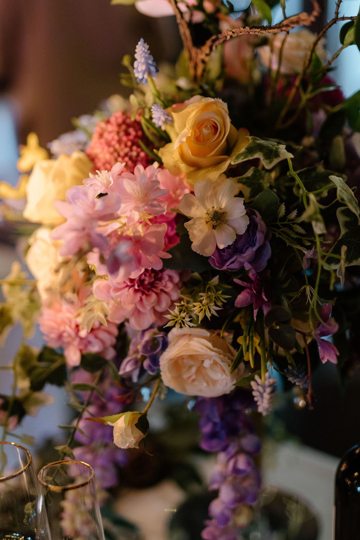 A romantic floral arrangement featuring peach roses, pink carnations, and purple wildflowers in soft lighting.