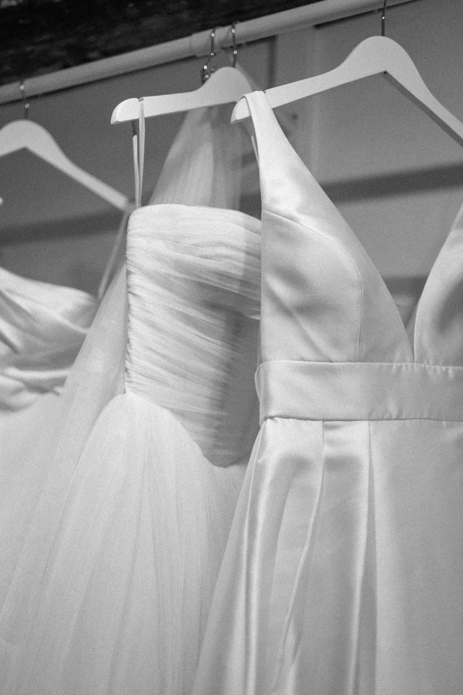 White wedding gowns with pleated bodices and different styles including tulle and satin fabrics hanging on dress hangers.