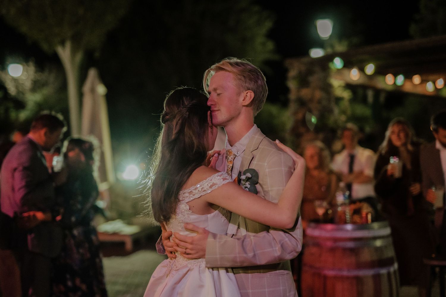Bride and groom sharing romantic first dance embrace at outdoor evening wedding reception.