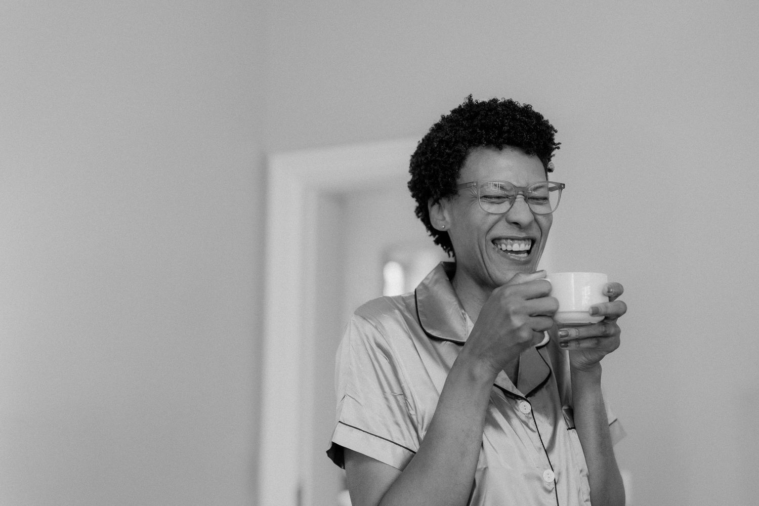 Woman laughing joyfully while holding a coffee cup in a black and white portrait photo.
