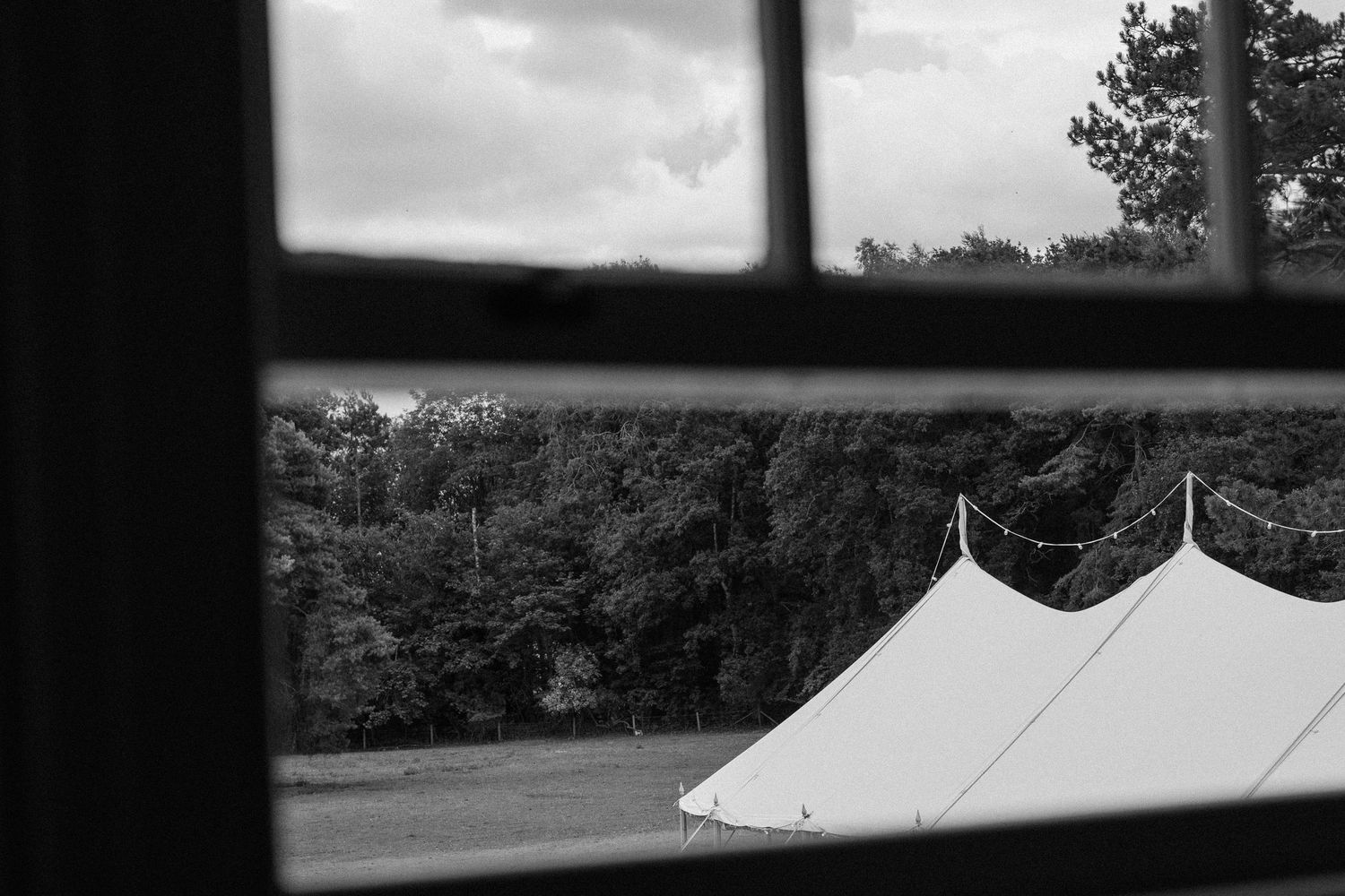 Black and white view of a white wedding tent through a window frame.