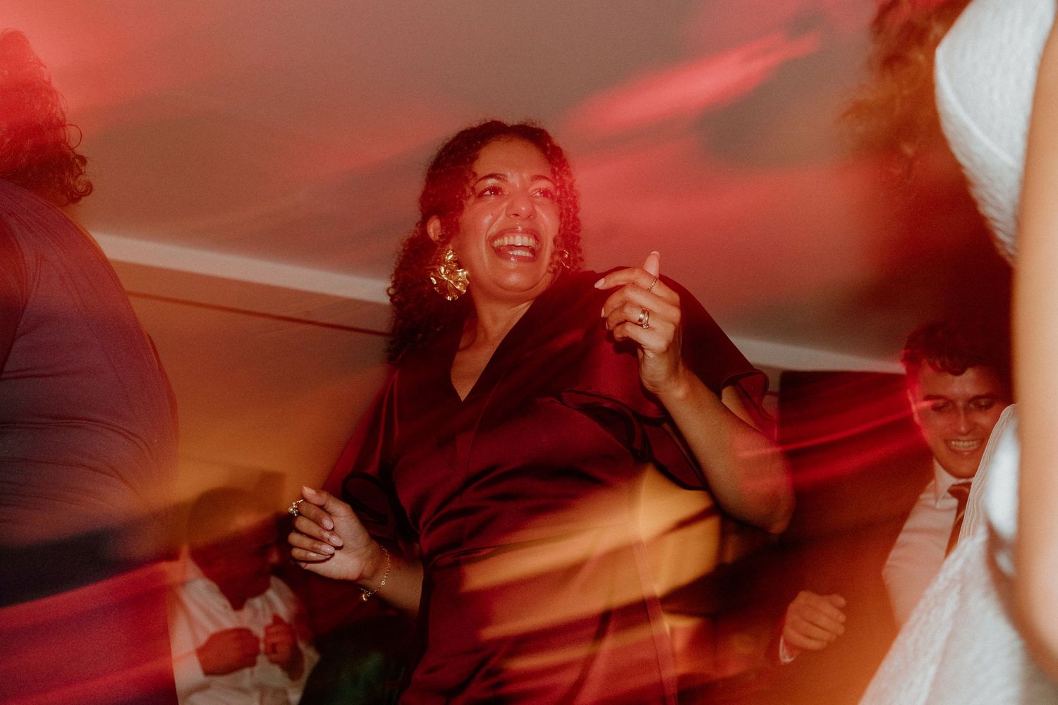 Guest in red dress dancing joyfully under red lights at a lively wedding reception.