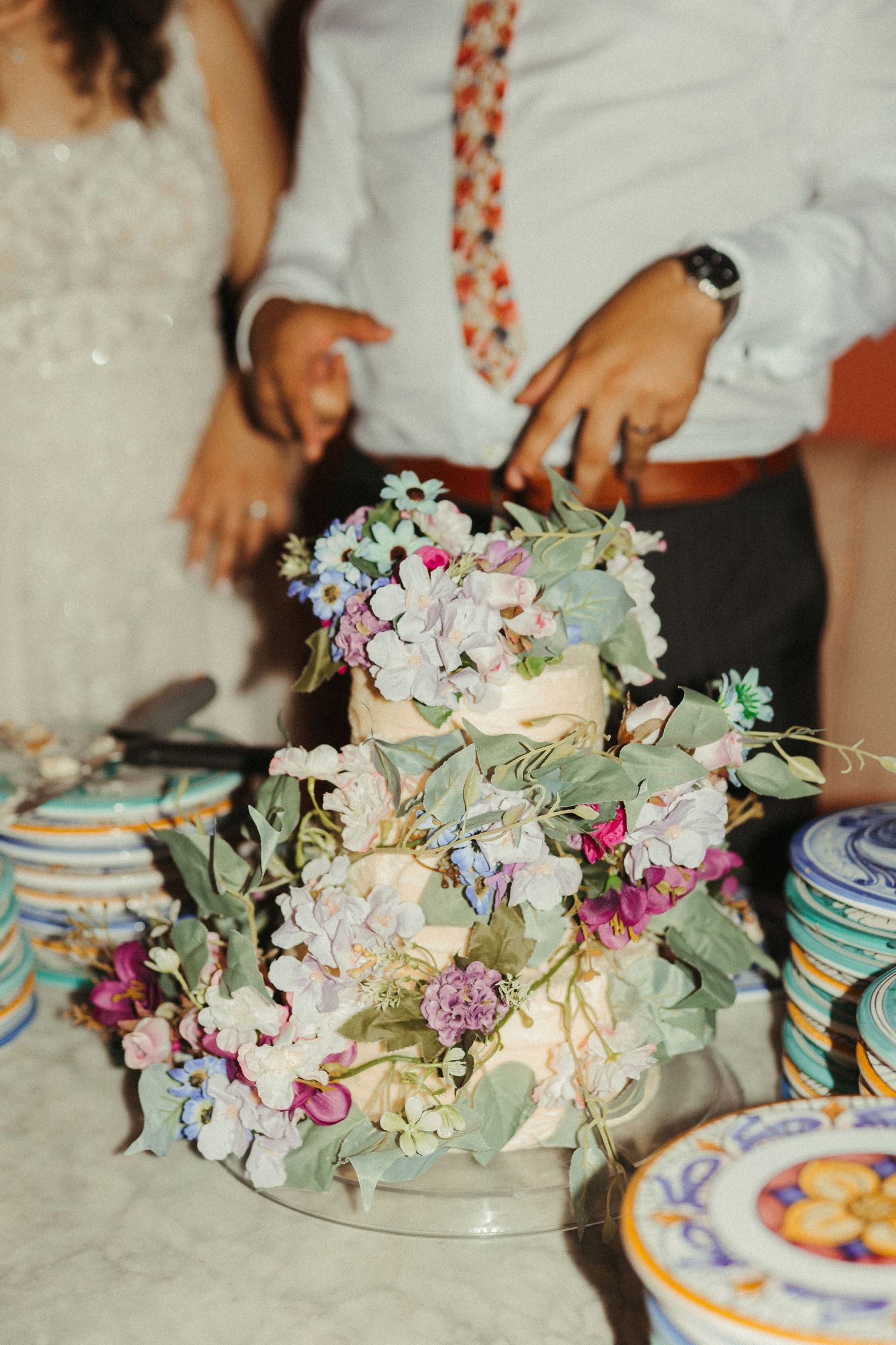 Elegant multi-tiered wedding cake adorned with colorful flowers and greenery on a marble table.