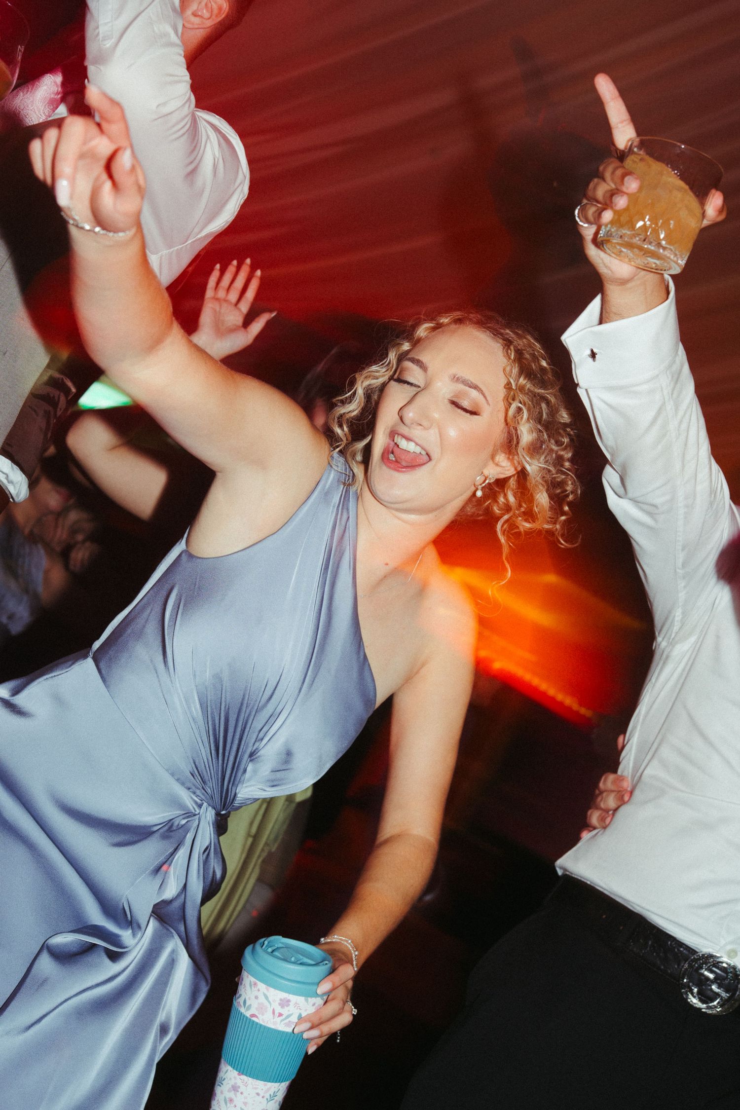 Bridesmaid in blue satin dress dancing energetically at a wedding reception.