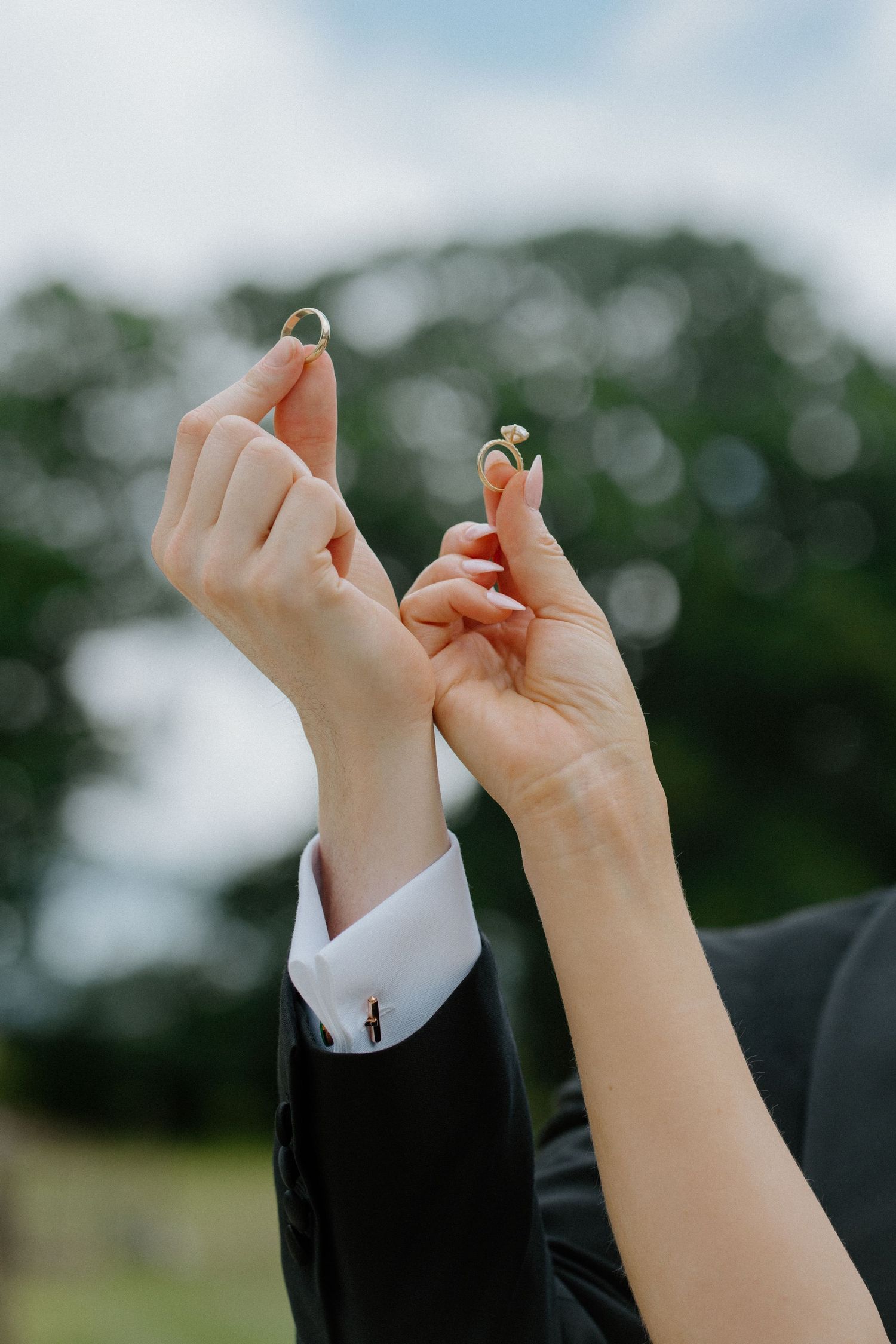 Bride and groom holding up their wedding rings against a green outdoor background after ceremony.