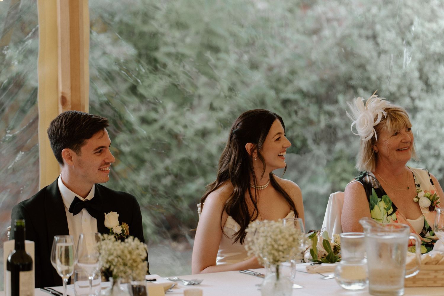 Bride and groom laughing at wedding reception head table with elegant floral arrangements.