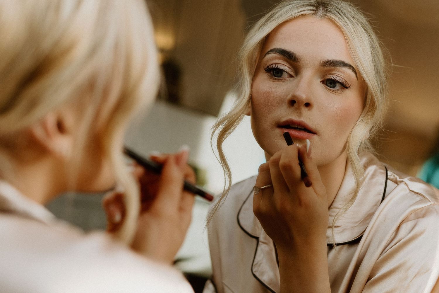 Close-up of makeup artist applying lipstick to blonde bride during wedding morning preparations.